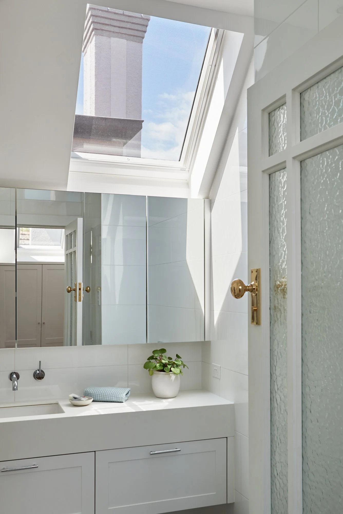 Upstairs bathroom with skylight, mirrored wall, white vanity and textured glass door at Adella Court, Elwood.
