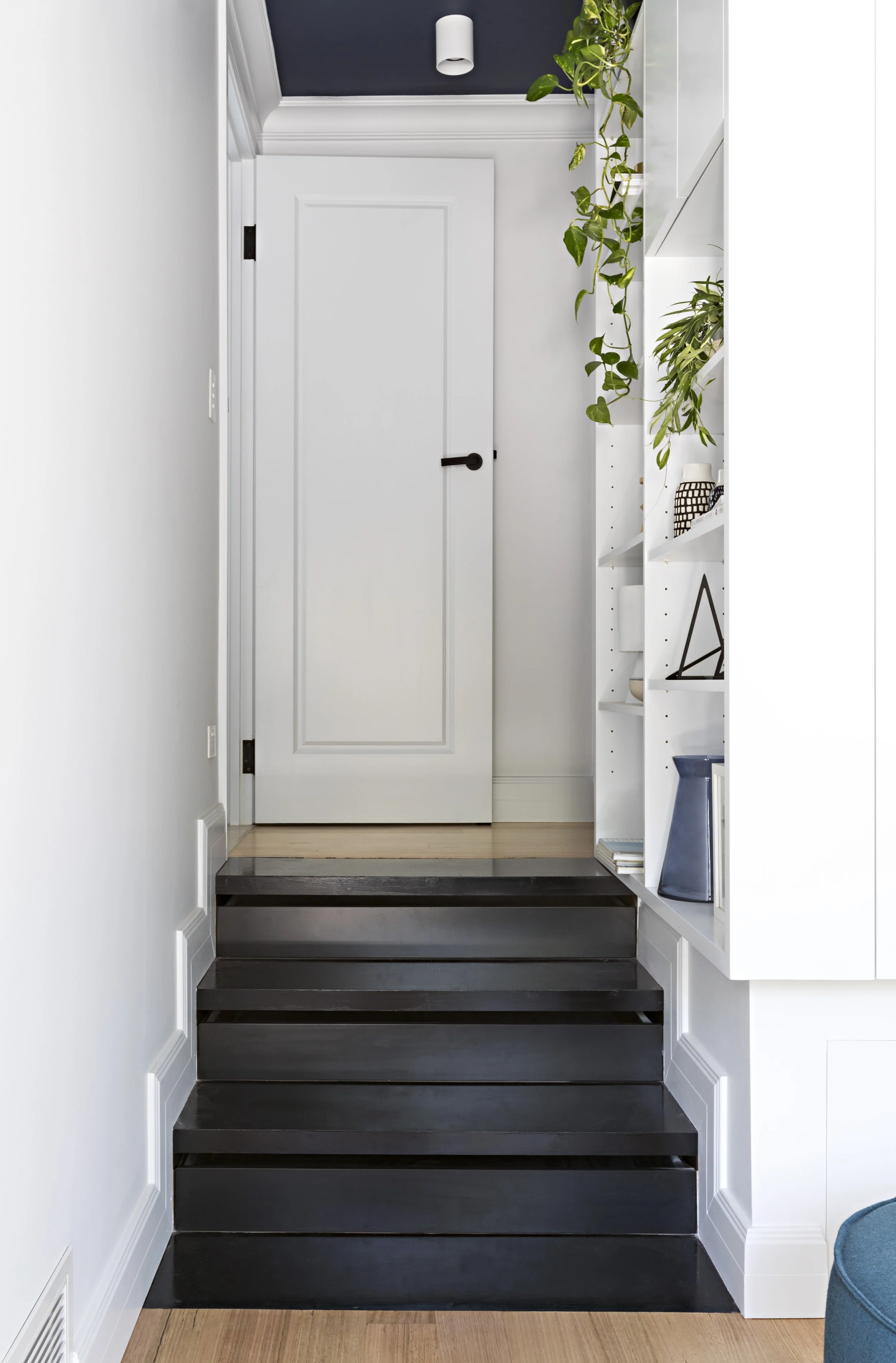 Black timber steps leading to a white door beside built-in shelving.