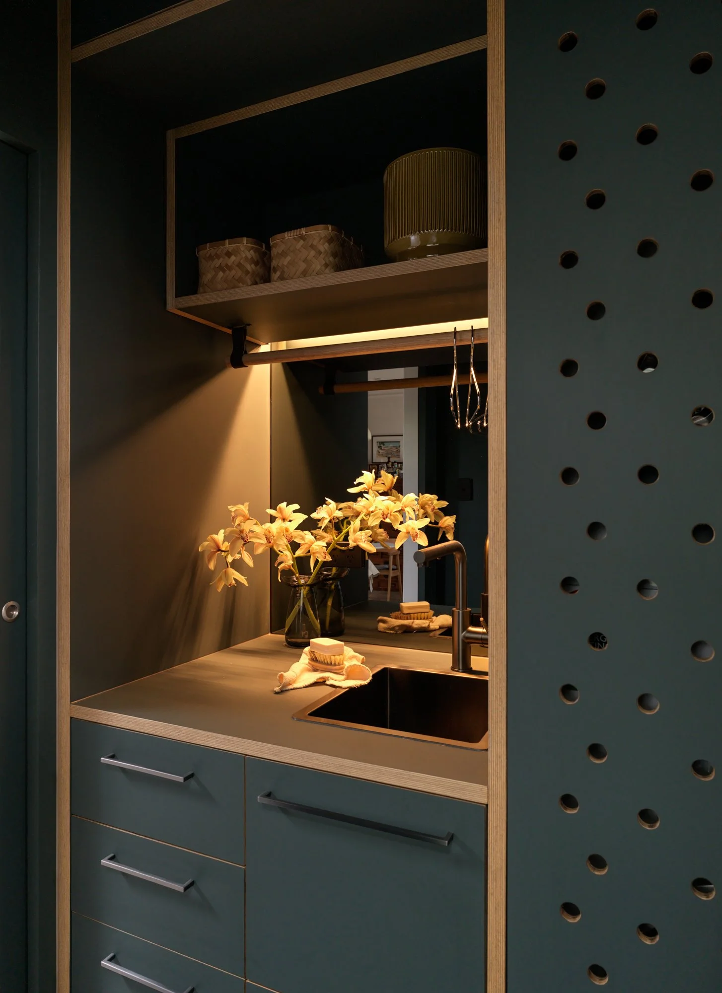 Brunswick Laundry with deep green cabinetry, integrated sink, open shelving and perforated storage doors.
