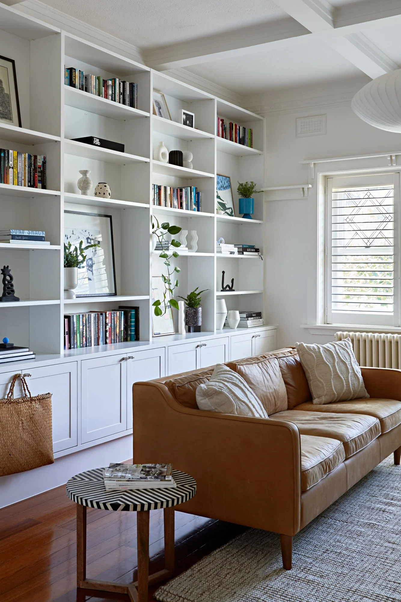 Living area with custom wall-to-wall shelving, leather sofa, timber floors and original window detailing at Adella Court, Elwood.