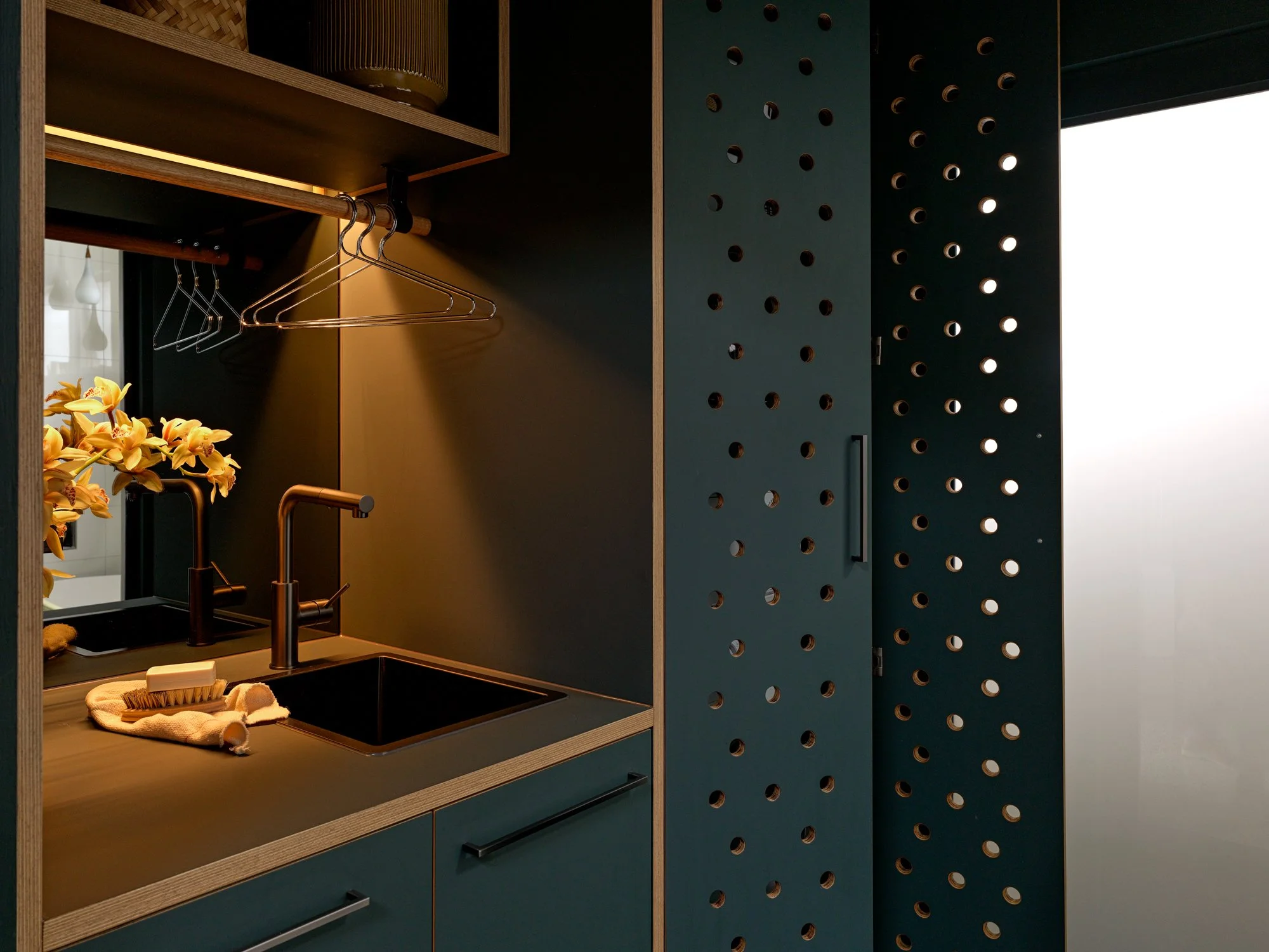Detail of the perforated green cabinetry in Brunswick Laundry beside the integrated sink and hanging rail.
