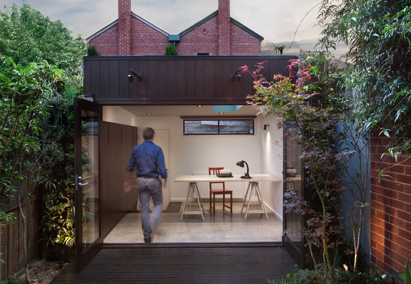Garden studio with dark timber cladding, large open glass doors and a simple workspace overlooking the landscaped courtyard.