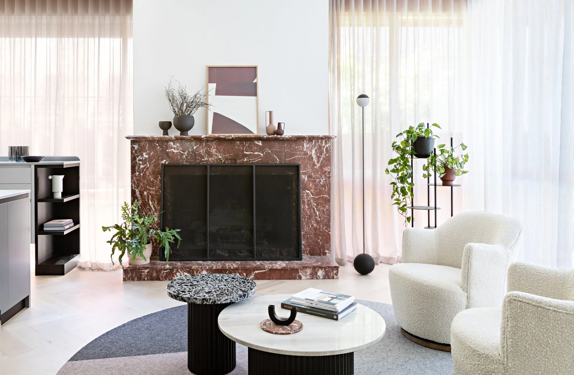 Light-filled living room with red marble fireplace, sheer curtains and curved armchairs at Brighton East House.