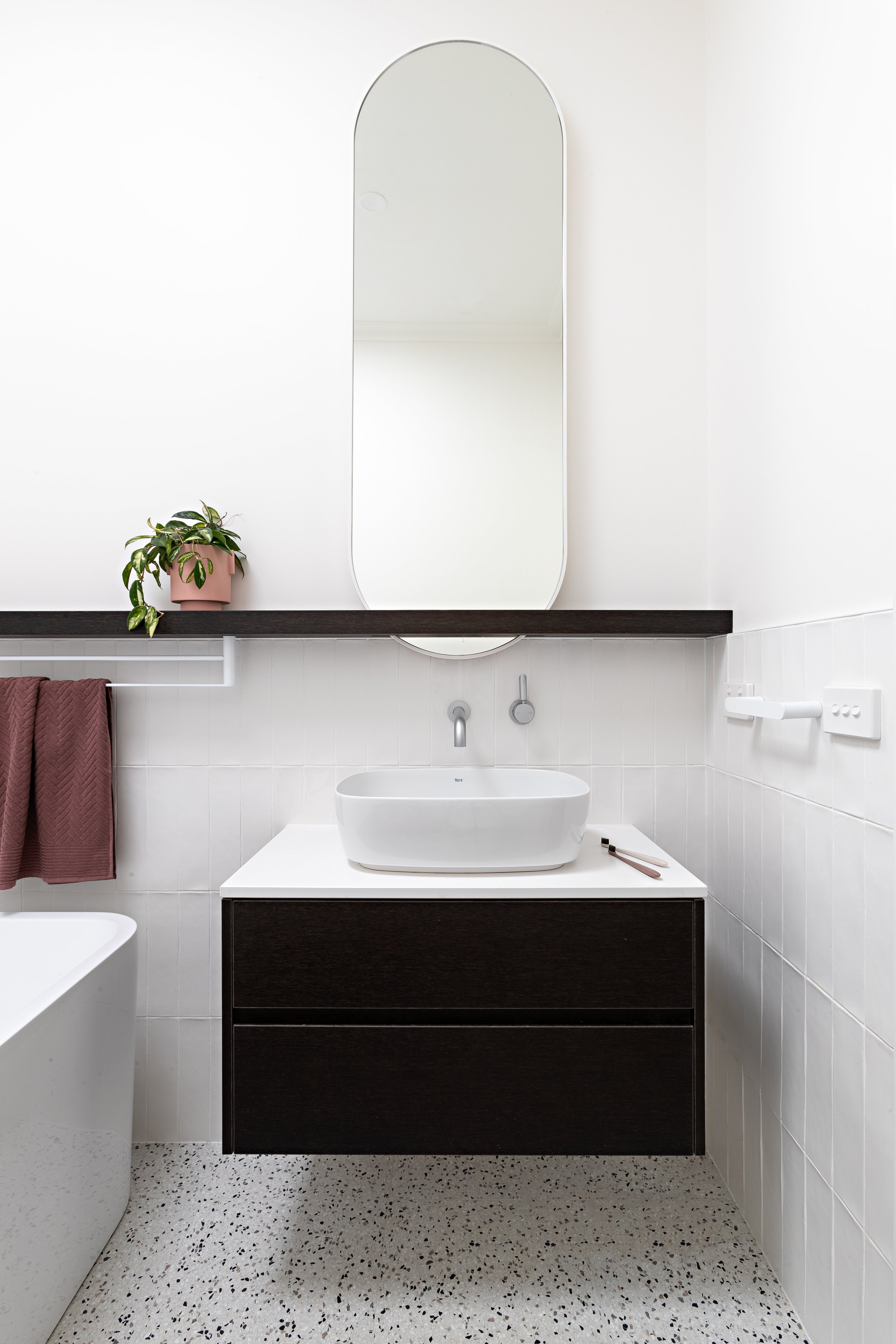 Front view of the bathroom vanity with dark timber cabinetry and tall oval mirror at Brighton East House.