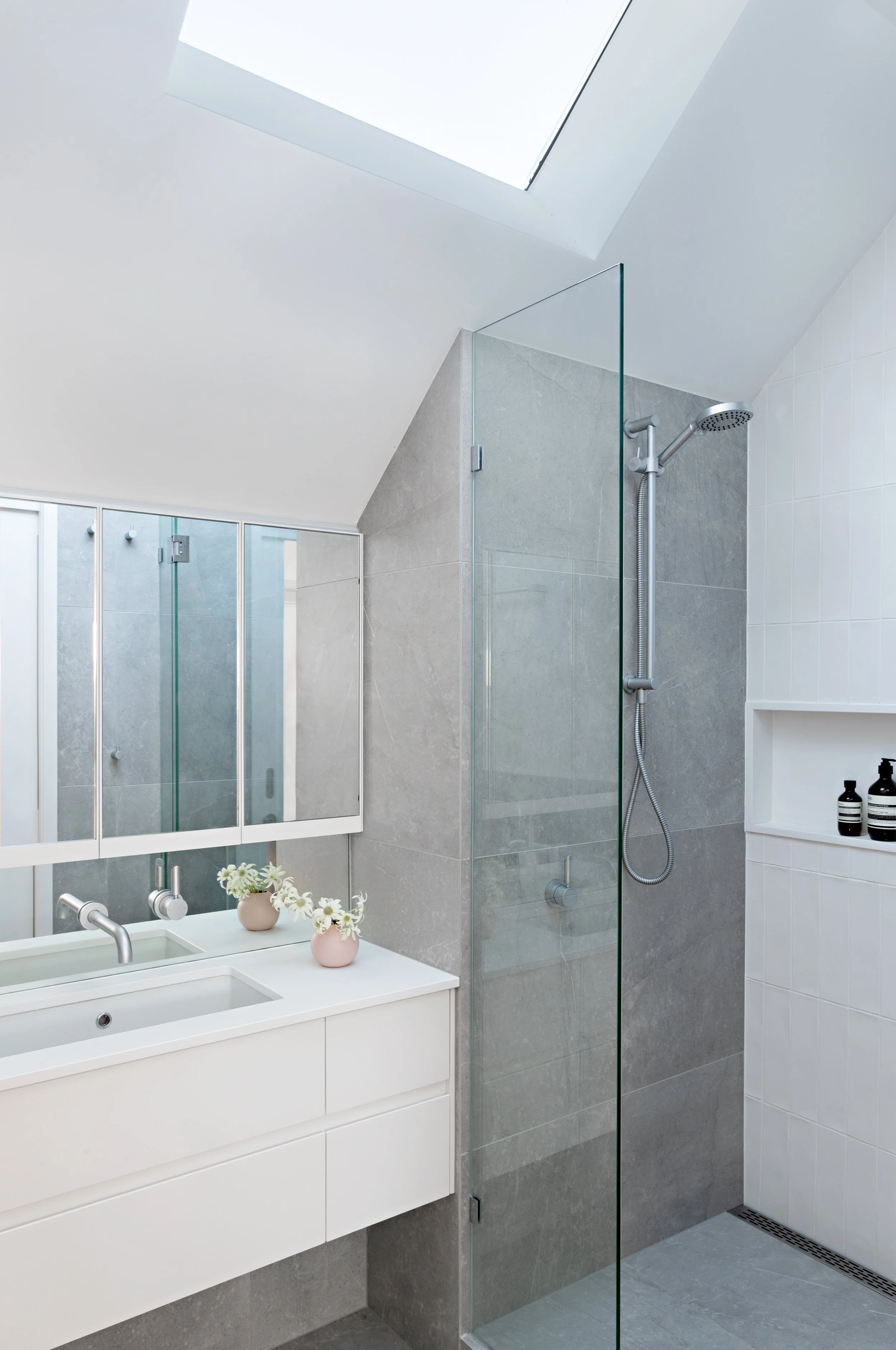 Brighton East House bathroom with frameless glass shower, grey tiles, white vanity and skylight.