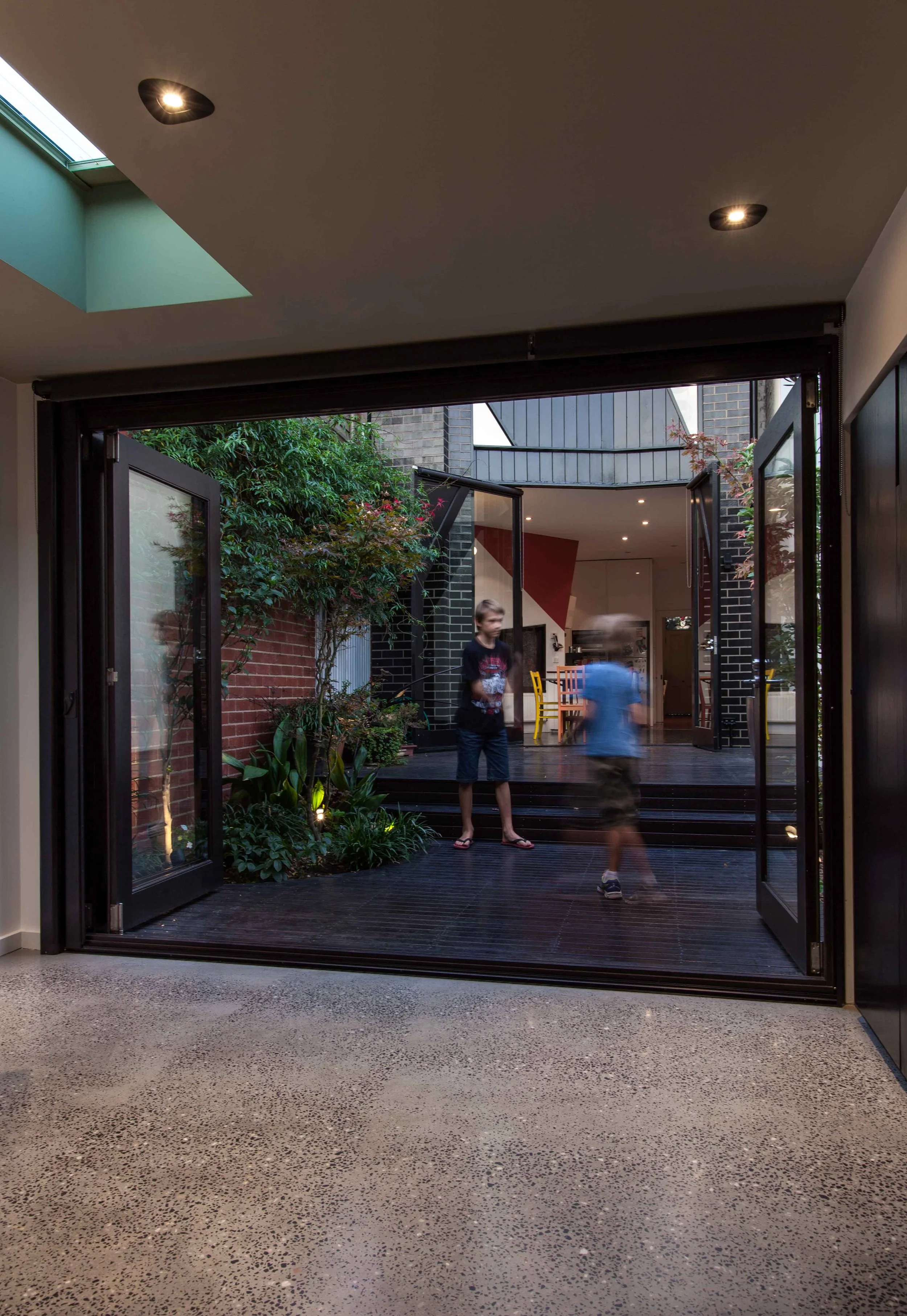 View from inside the garden studio through open glass doors to a planted courtyard and adjoining home.