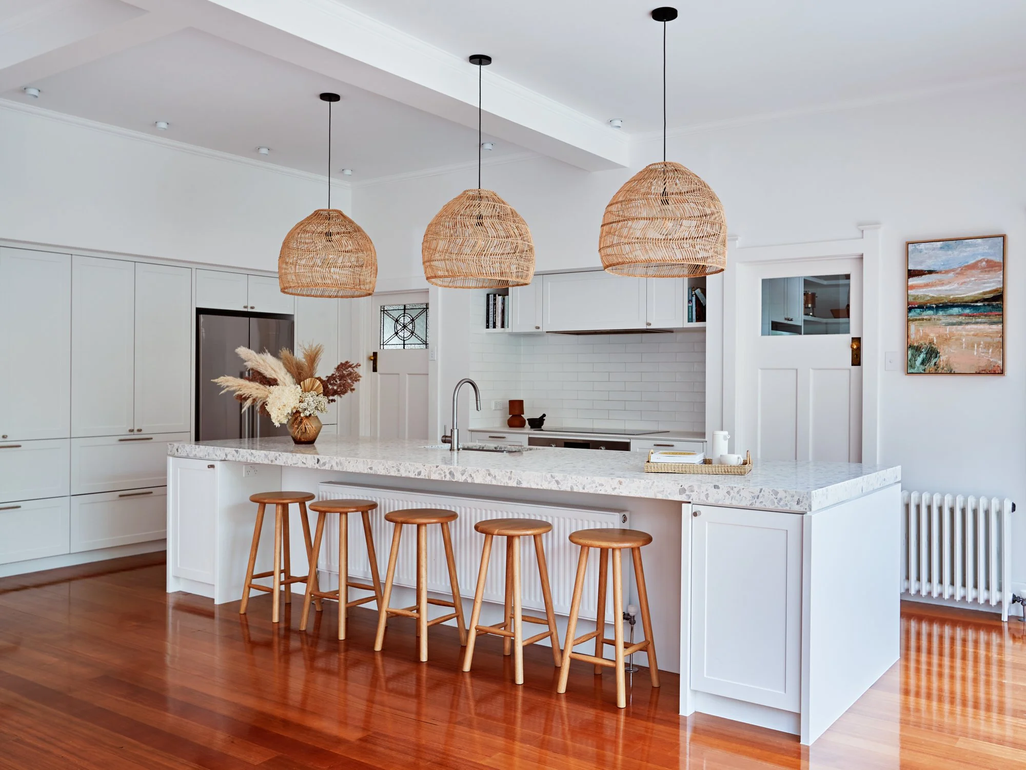 Renovated kitchen at Adella Court, Elwood with a large island bench, white cabinetry and woven pendant lights.