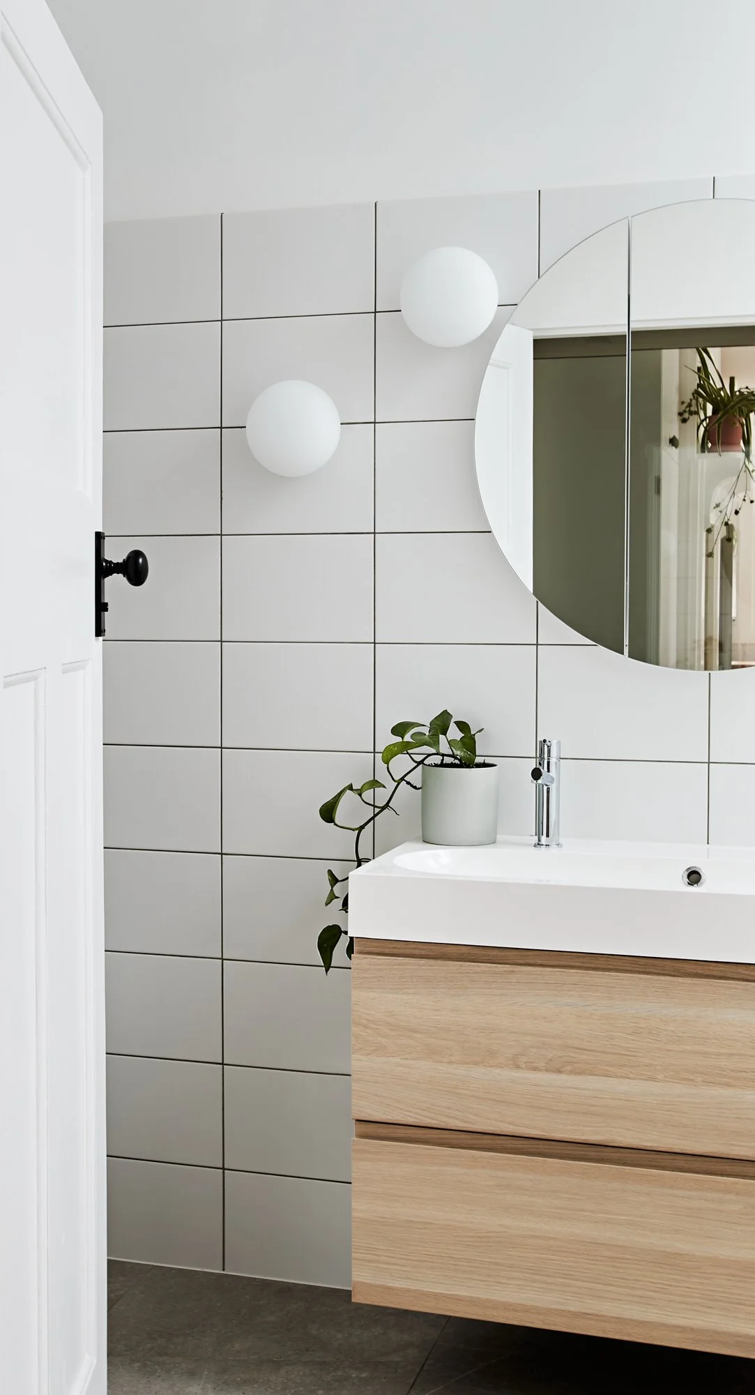 Bathroom vanity at Northcote Green House with timber cabinetry, white tiles, round mirror and wall lights.