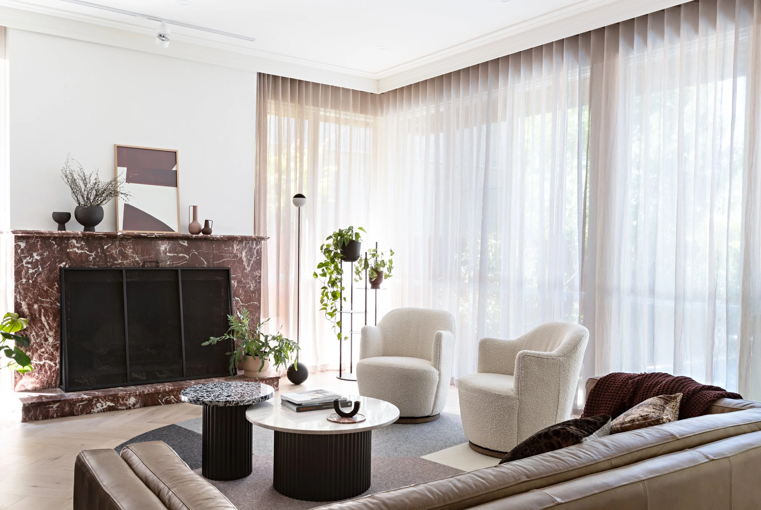 Brighton East House living room with red marble fireplace, curved seating and floor-to-ceiling sheer curtains.