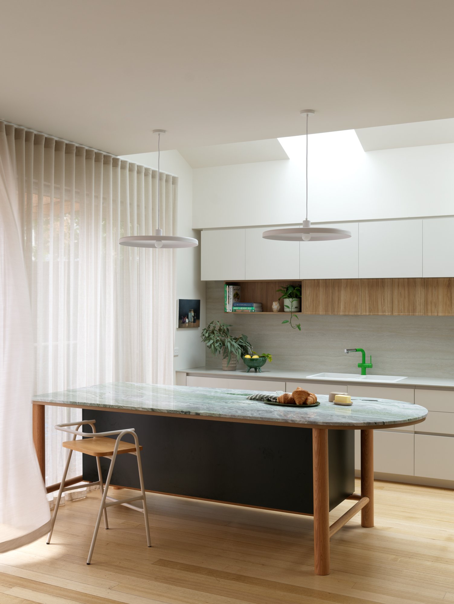 Kitchen island at Northcote Extension with a curved stone benchtop, timber legs and pendant lighting beneath the skylights.