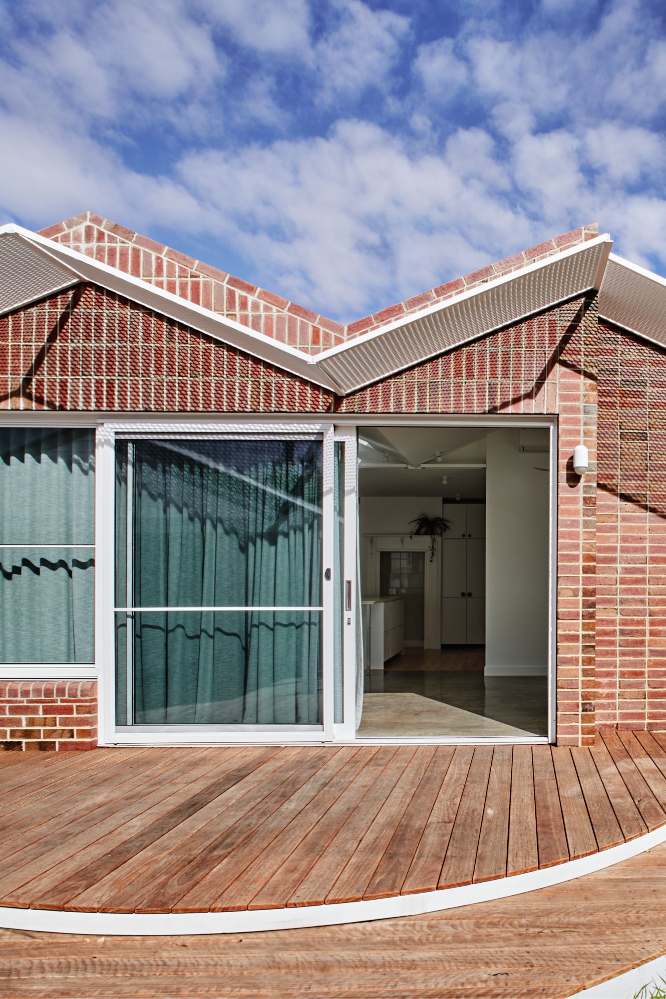 Rear entry to Northcote Green House with red brick walls, sliding glass door and curved timber deck.