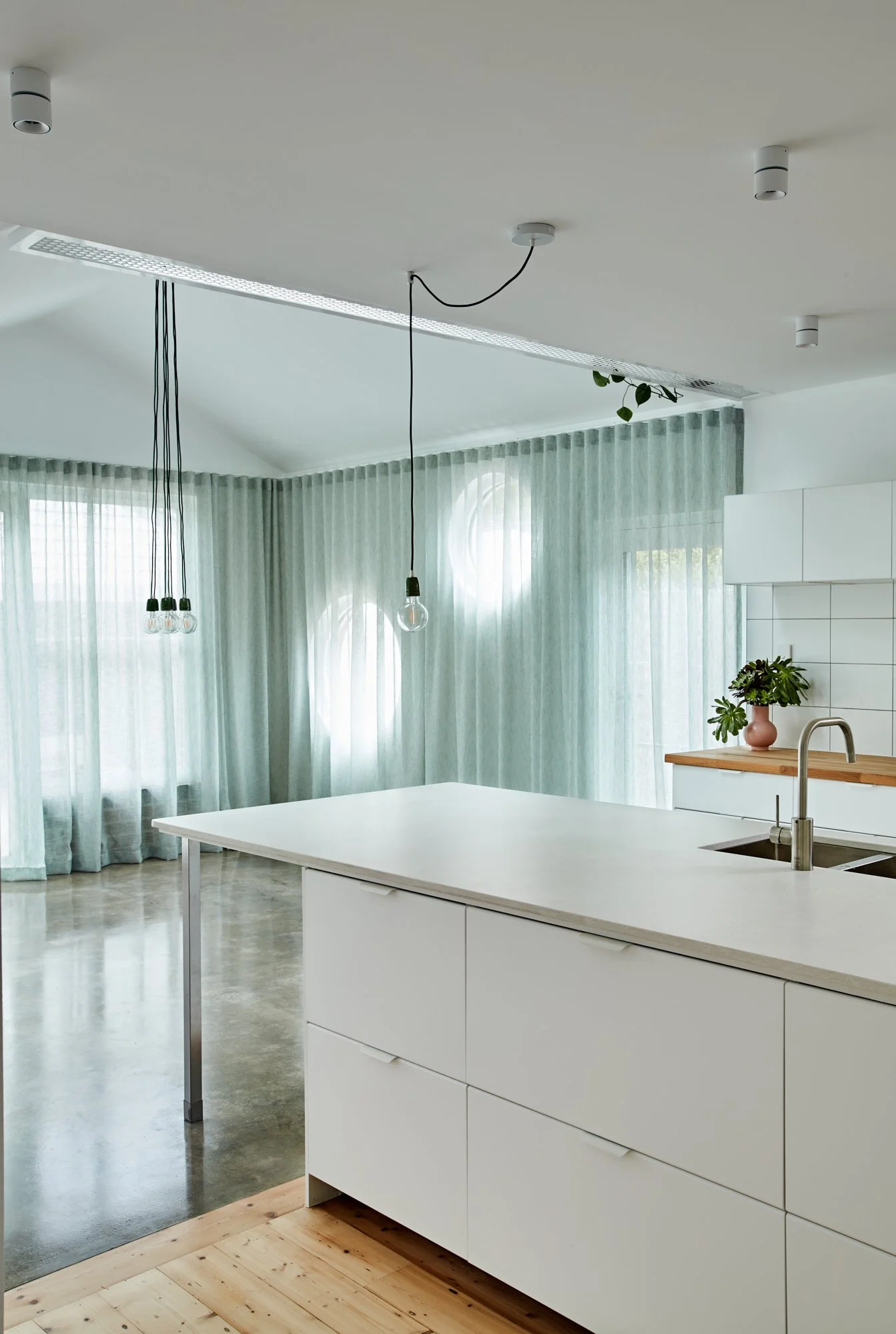 White kitchen and open-plan living area at Northcote Green House with green curtains and circular windows.