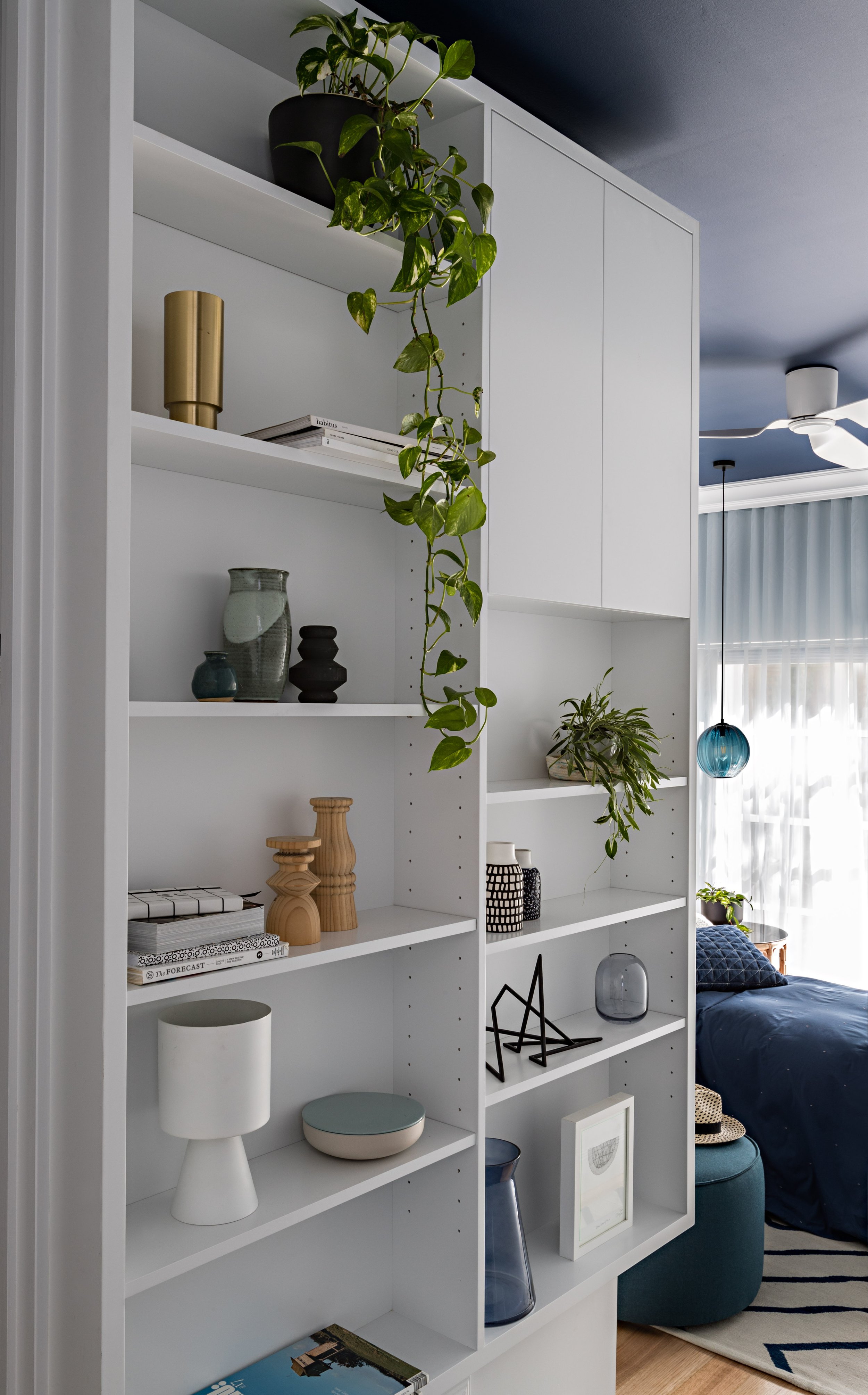 Floor-to-ceiling white shelving with integrated cabinetry, plants and display objects.