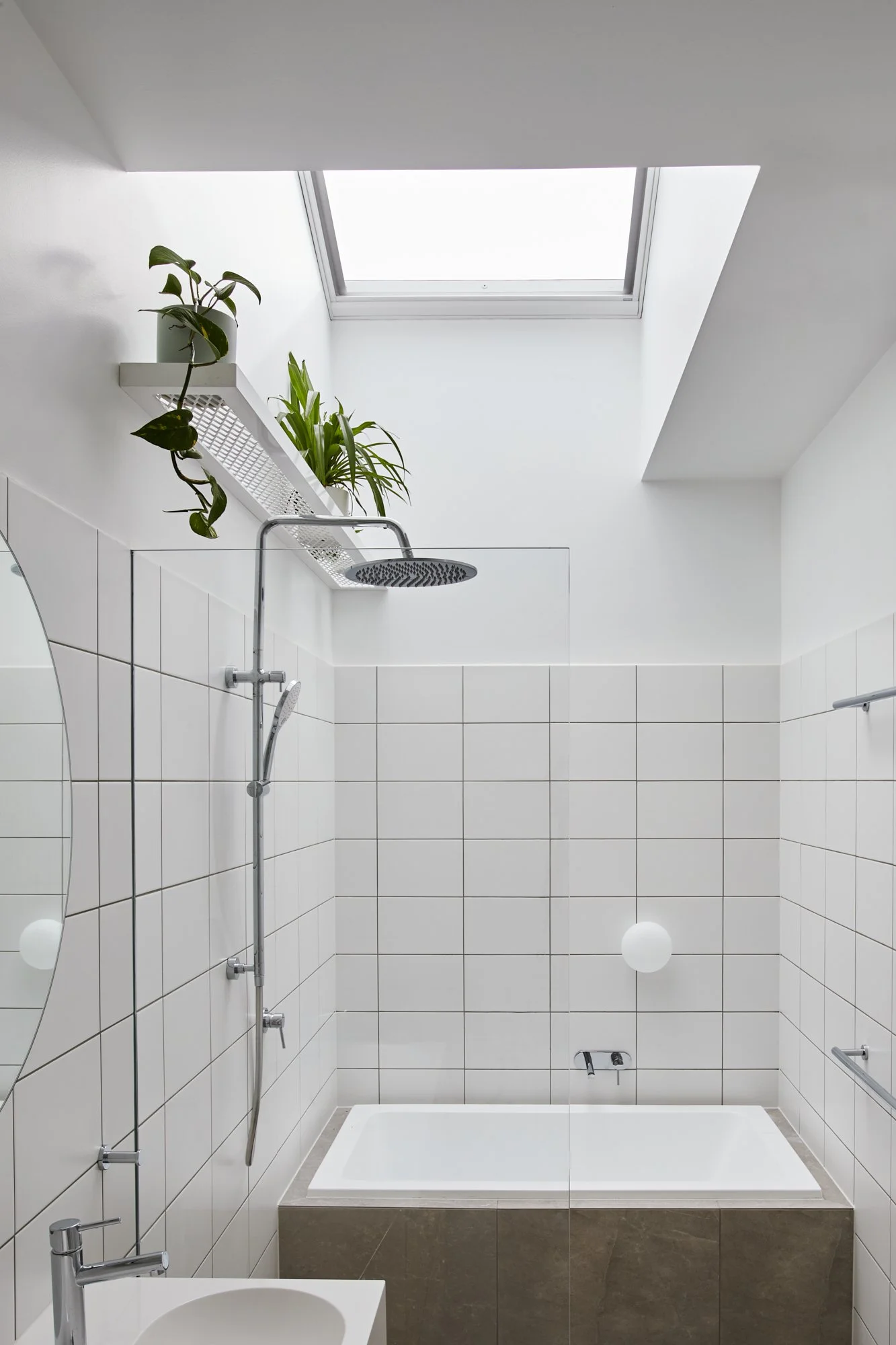 Bathroom at Northcote Green House with tiled bath, overhead shower, skylight and integrated plant shelf.