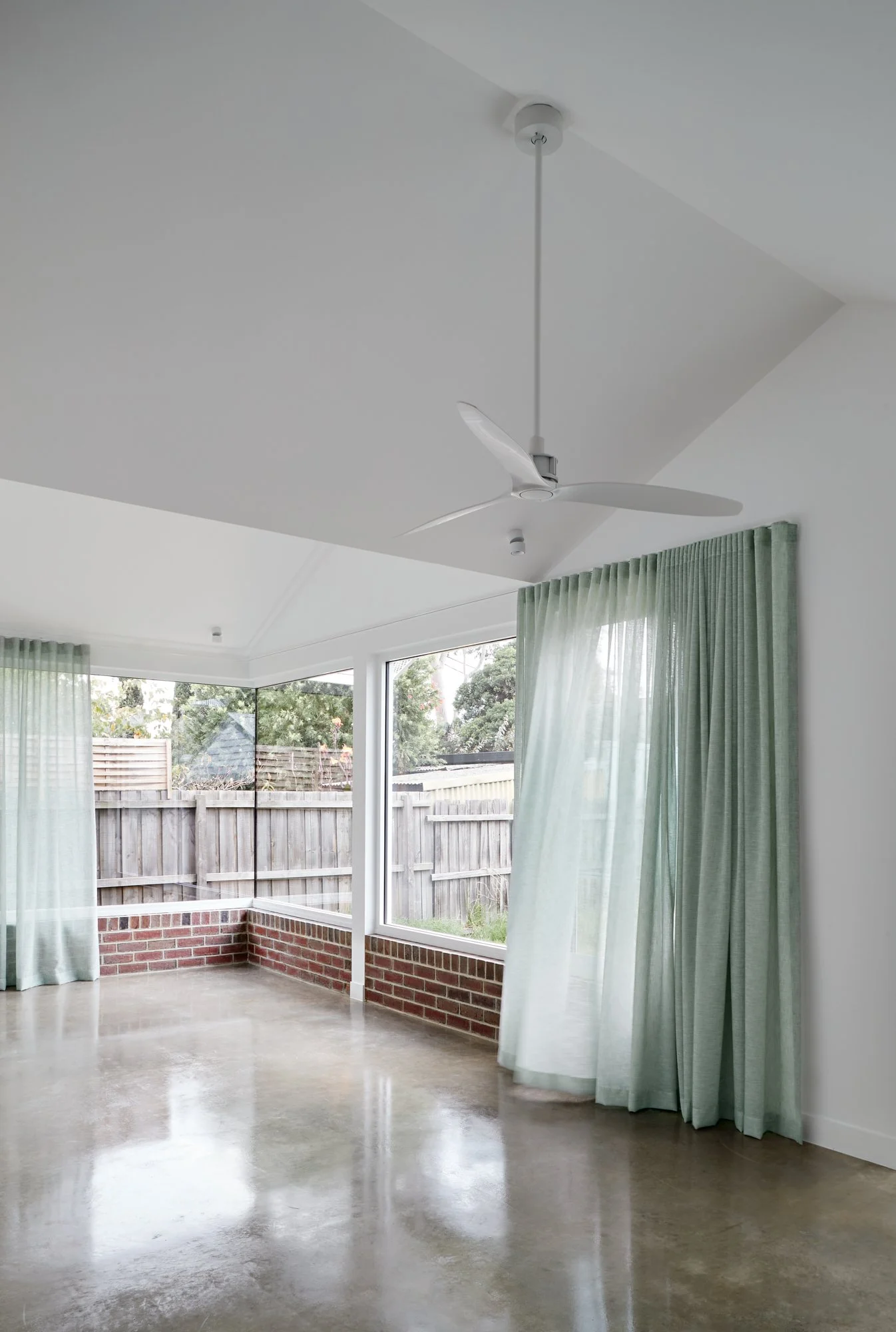 Living area at Northcote Green House with polished concrete floors, large windows and sheer green curtains.