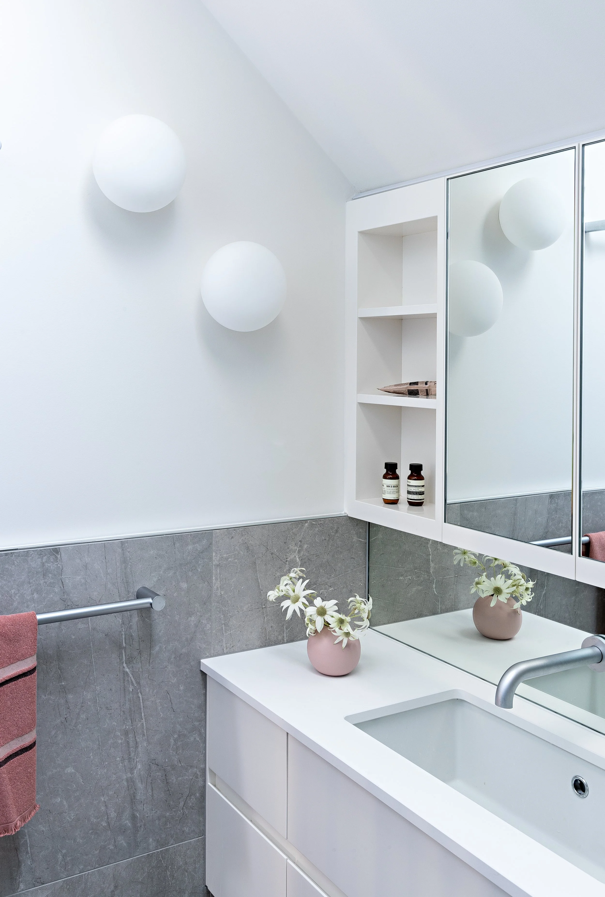 Light-filled bathroom with mirrored cabinetry, integrated basin and grey tiled walls at Brighton East House.