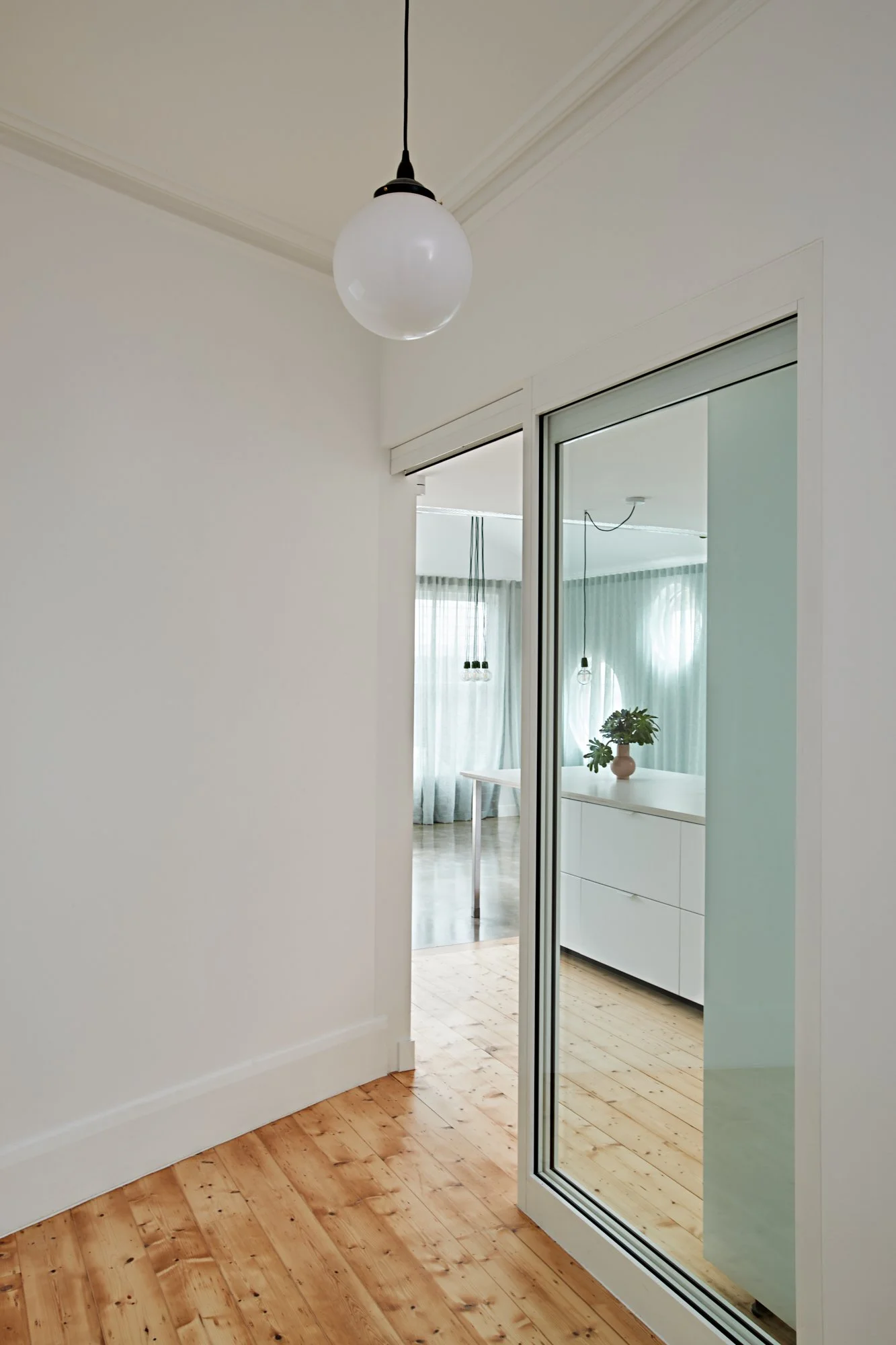 Interior transition at Northcote Green House showing timber flooring and a glazed sliding door opening to the kitchen and living area.