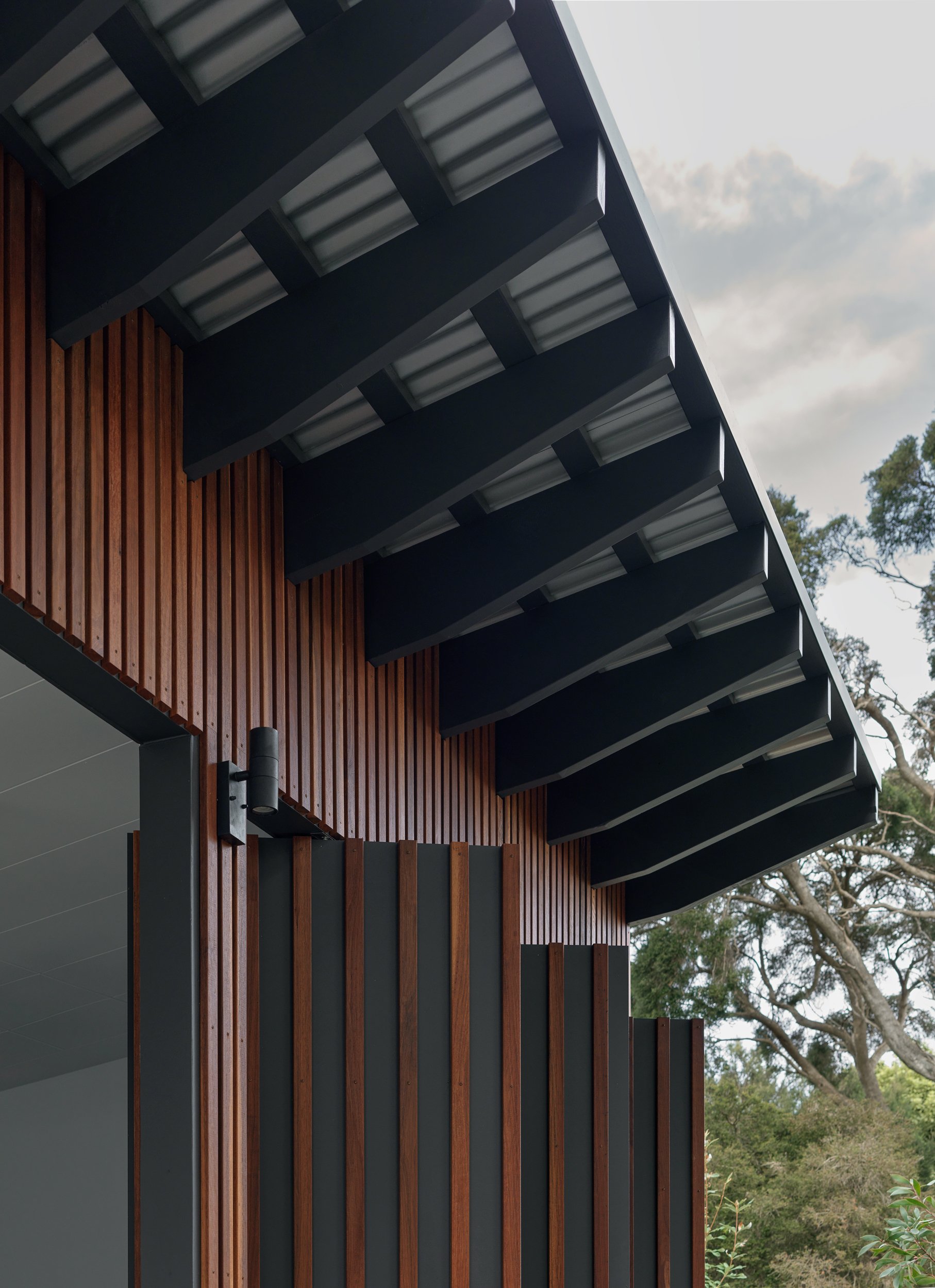 Close view of the Cottesloe Retreat roofline with exposed dark beams, vertical timber cladding and surrounding trees.