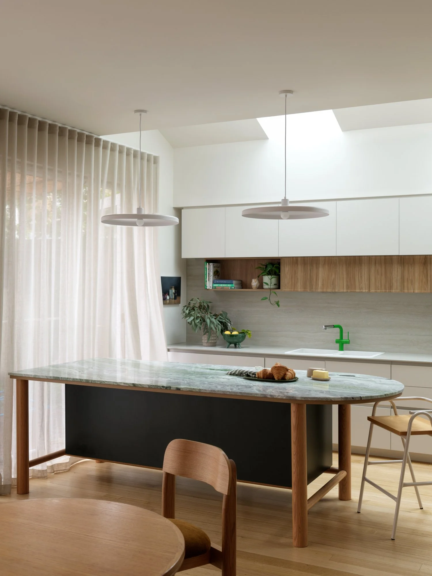 Northcote Extension kitchen and dining area with a curved stone island, timber flooring and natural light through sheer curtains.