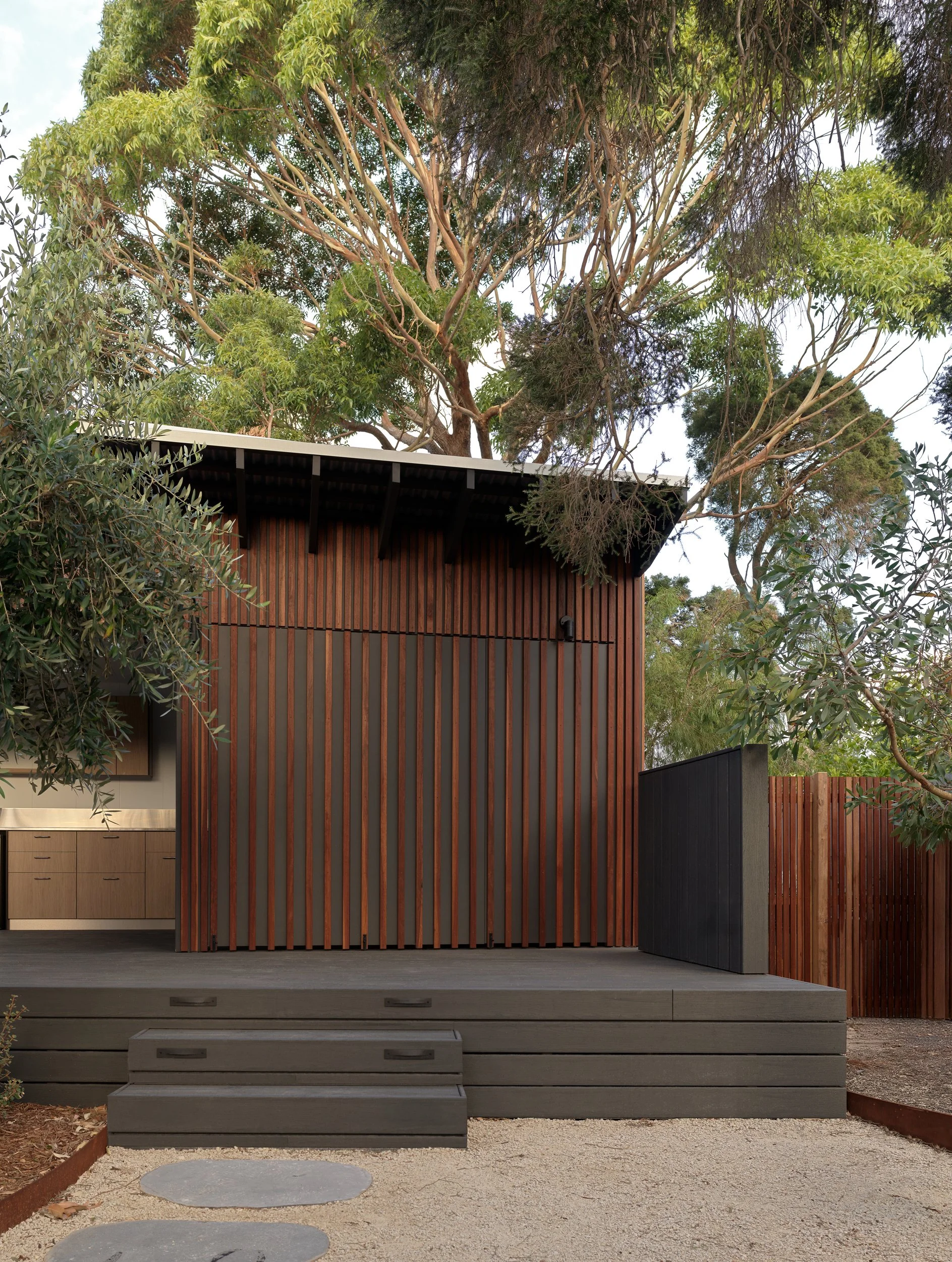 Cottesloe Retreat with its timber screens closed across the deck, framed by mature trees and surrounding bushland.