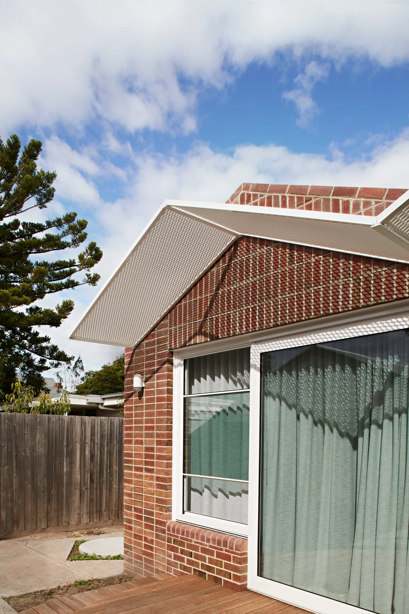 Detail of the red brick exterior and perforated metal roof screen at Northcote Green House.