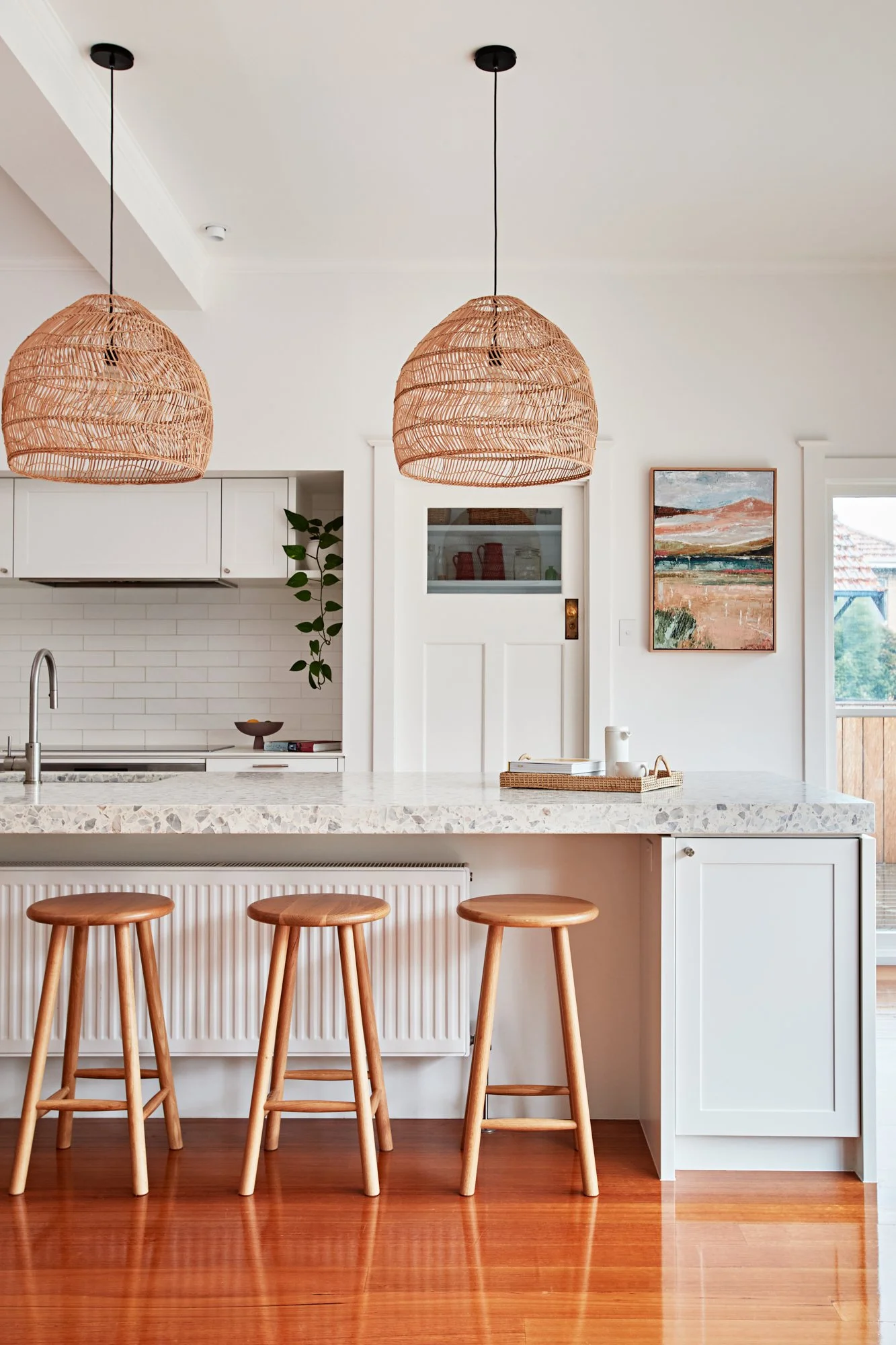 Kitchen island and dining area with white cabinetry, terrazzo benchtop and timber stools at Adella Court, Elwood.