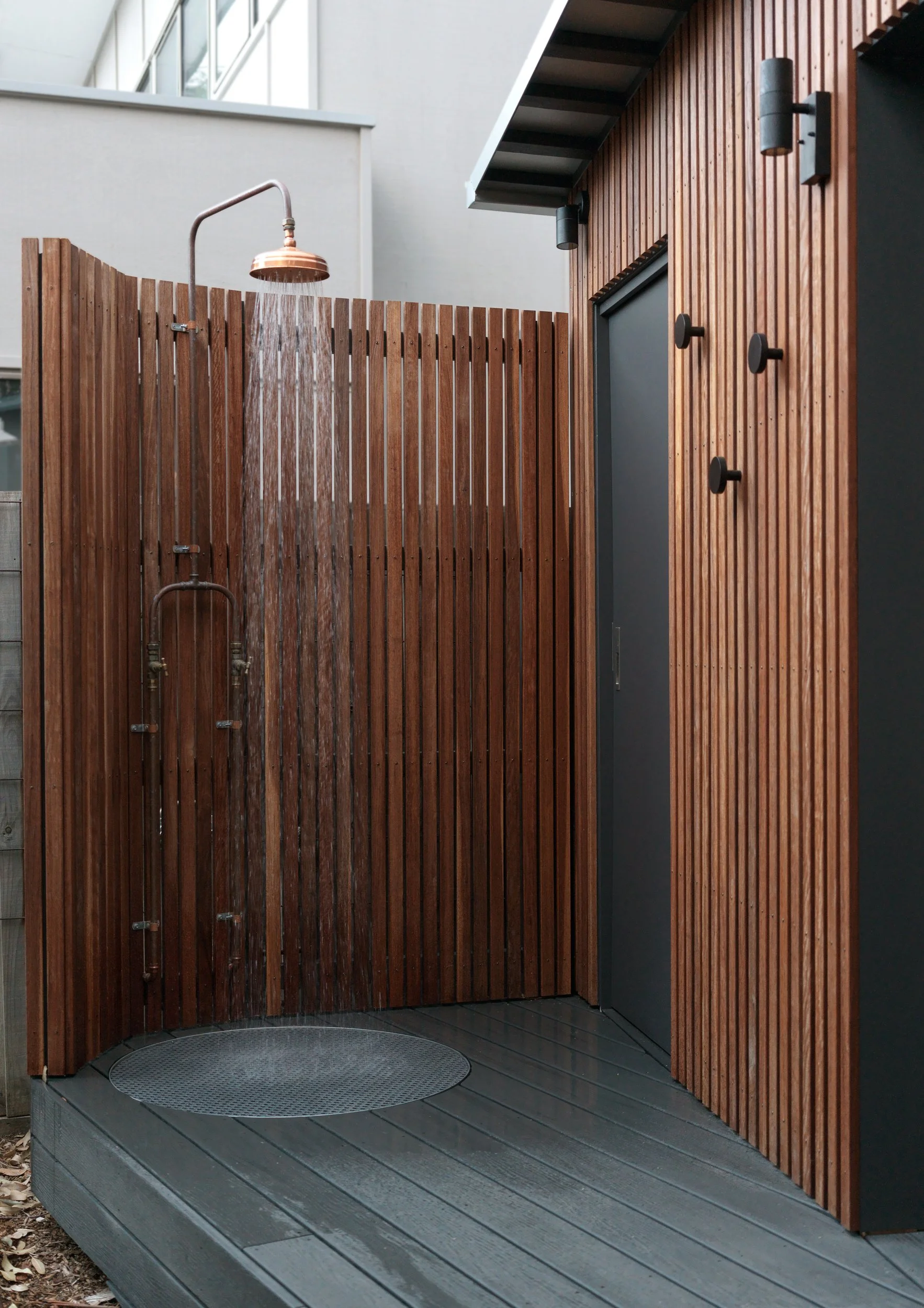 Outdoor shower at Cottesloe Retreat with copper fittings, timber screening and a dark deck underfoot.