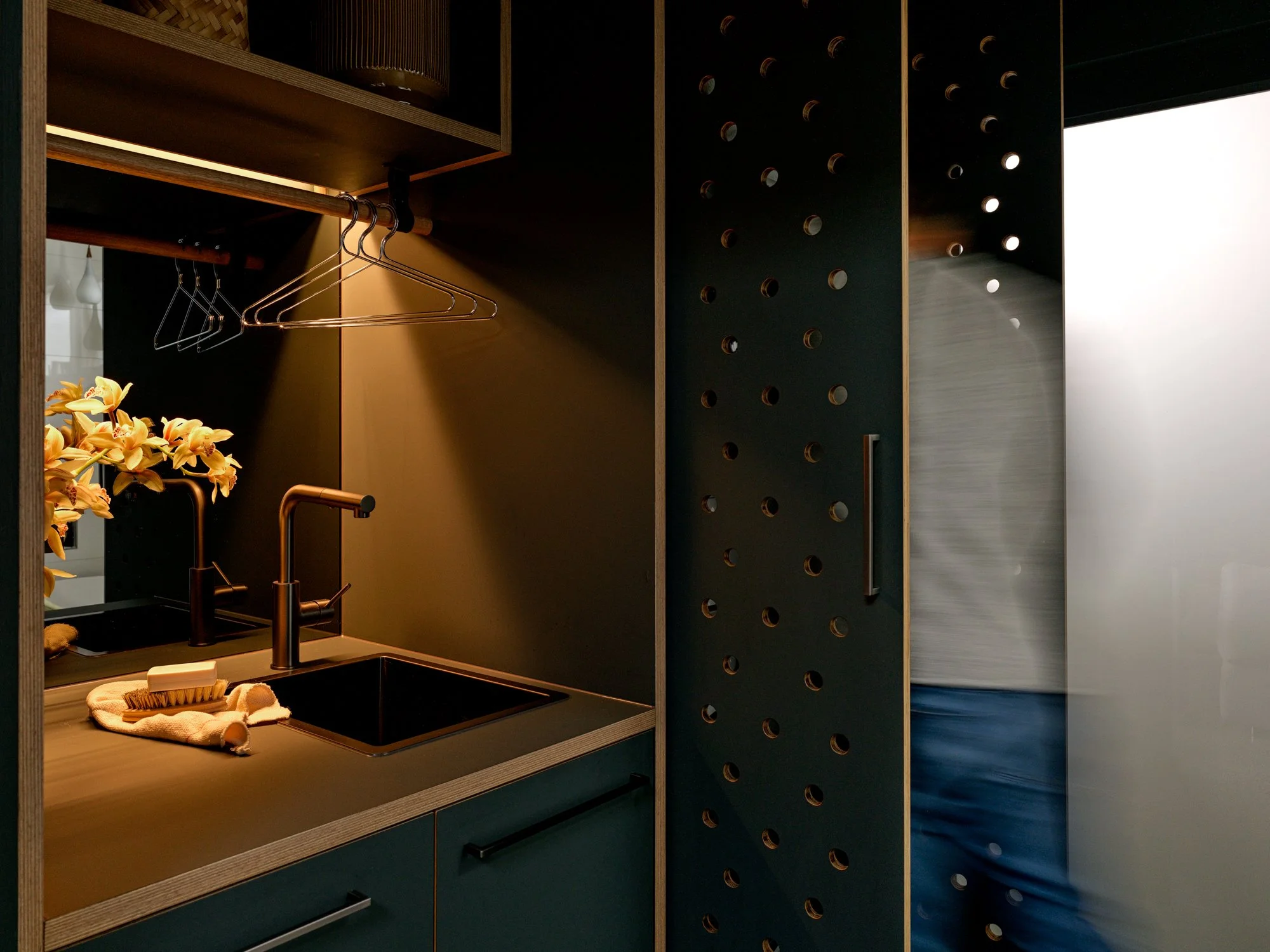 Brunswick Laundry with deep green cabinetry, integrated sink and perforated doors opening towards the adjoining space.