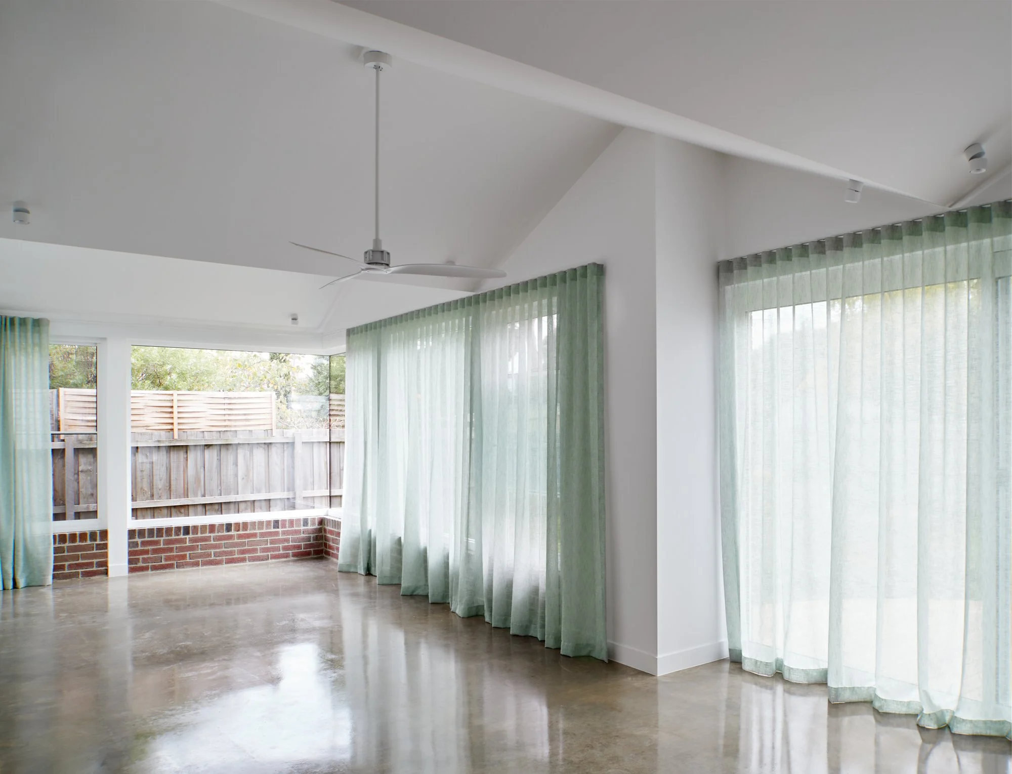 Open living space at Northcote Green House with polished concrete floors, green curtains and large windows.