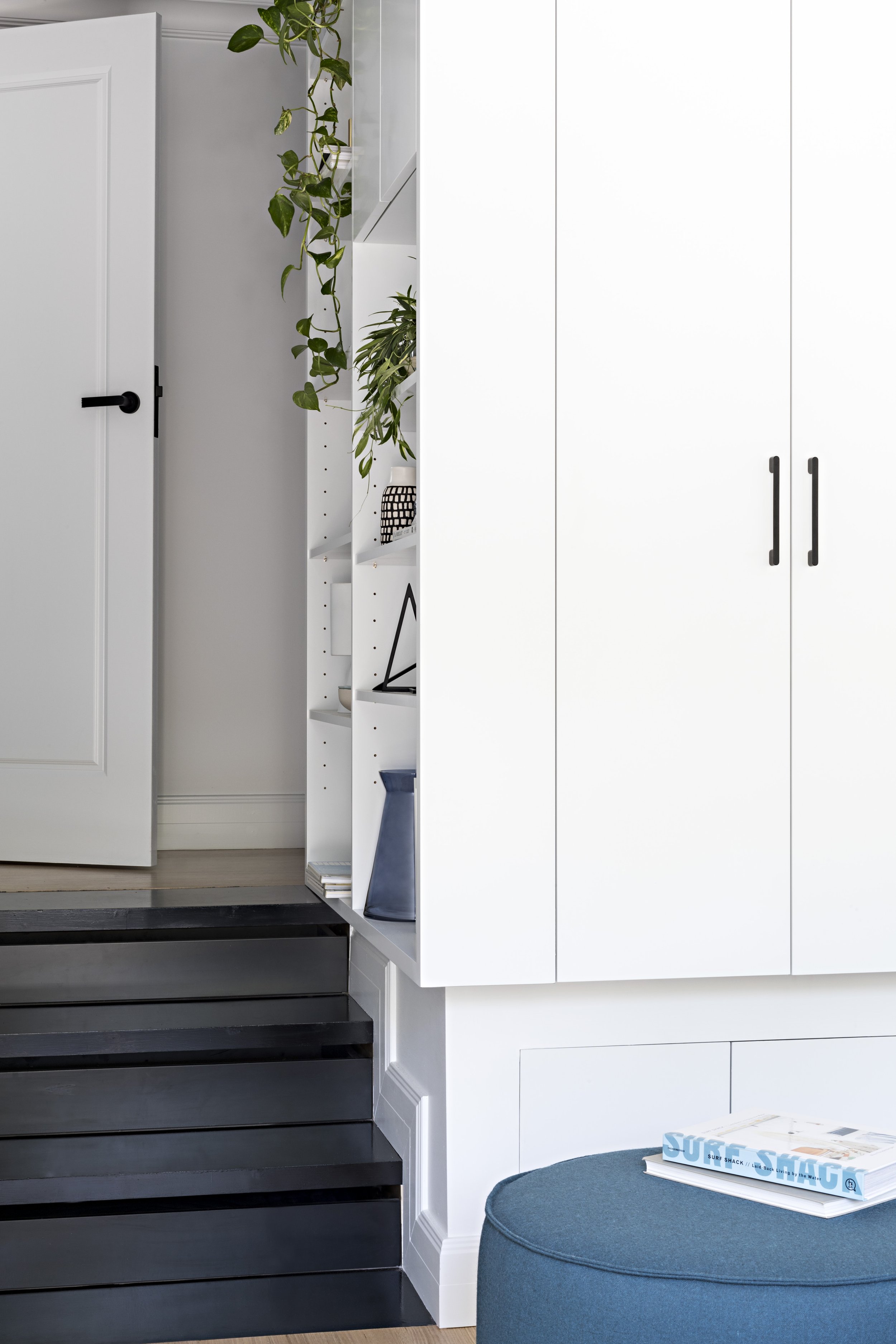 White built-in bedroom cabinetry and shelving beside black timber steps.