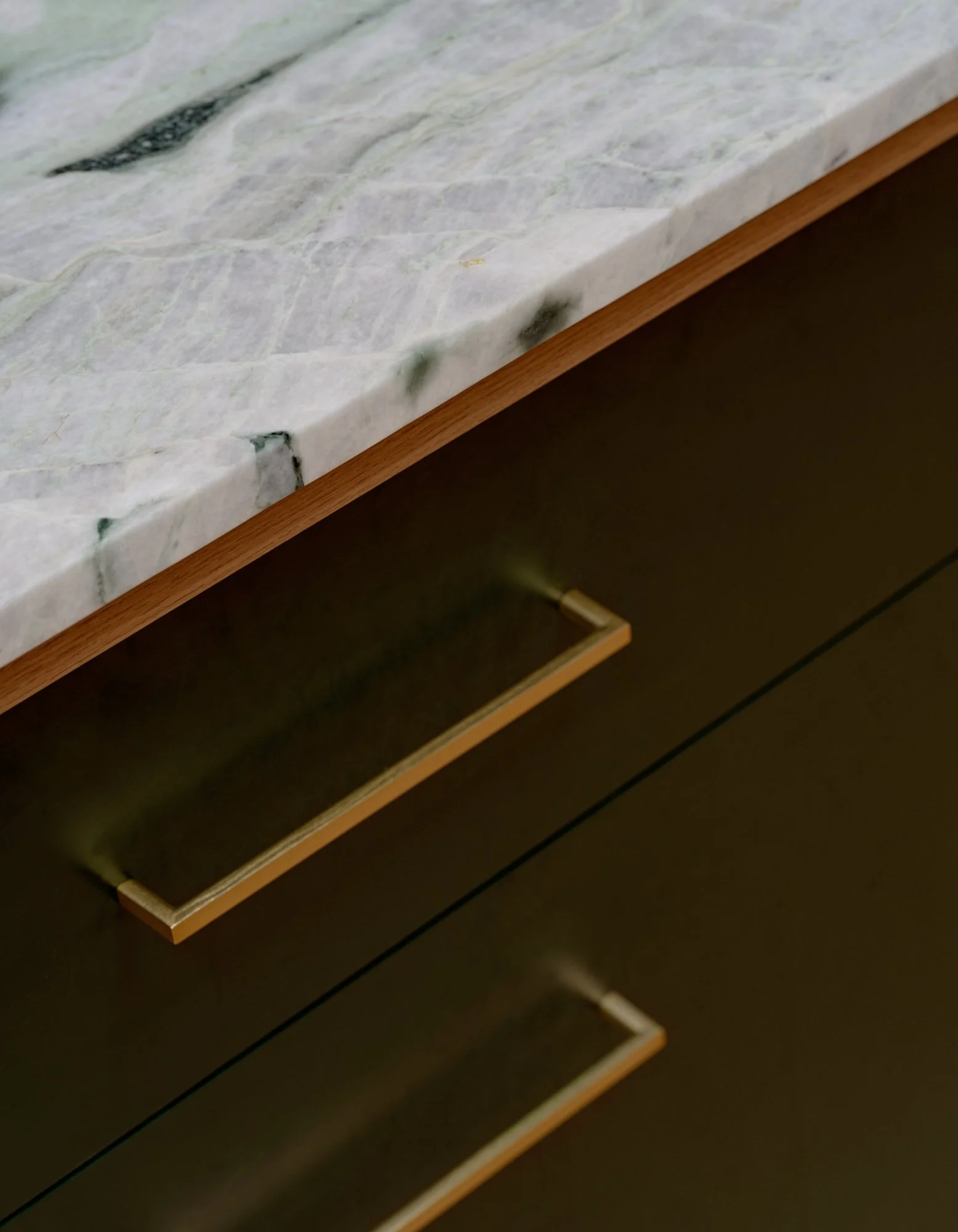 Close-up of the Northcote Extension kitchen island showing the stone benchtop, timber edge and brass cabinet handles.