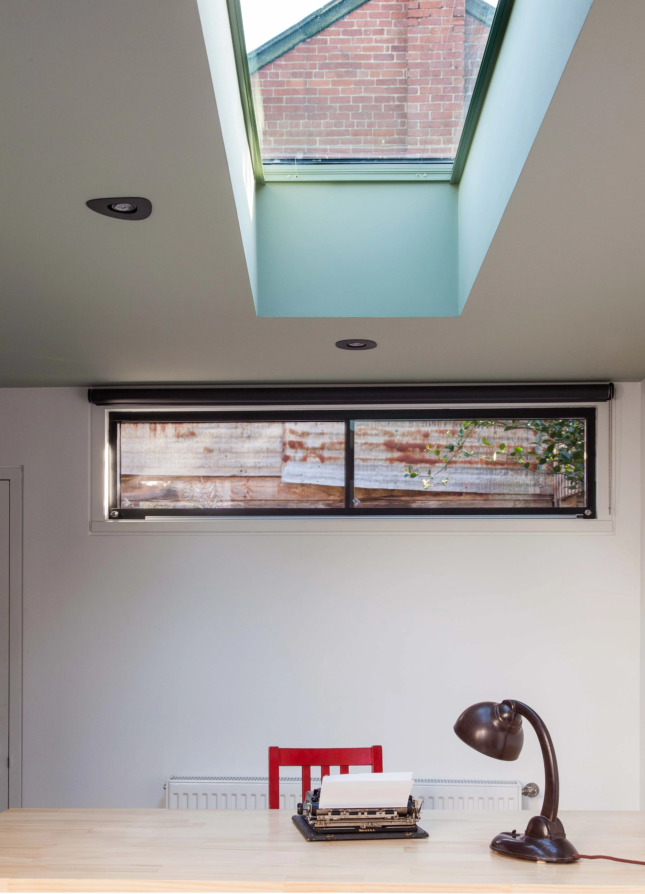 Interior workspace with a large skylight, horizontal window, timber desk, red chair and vintage typewriter.