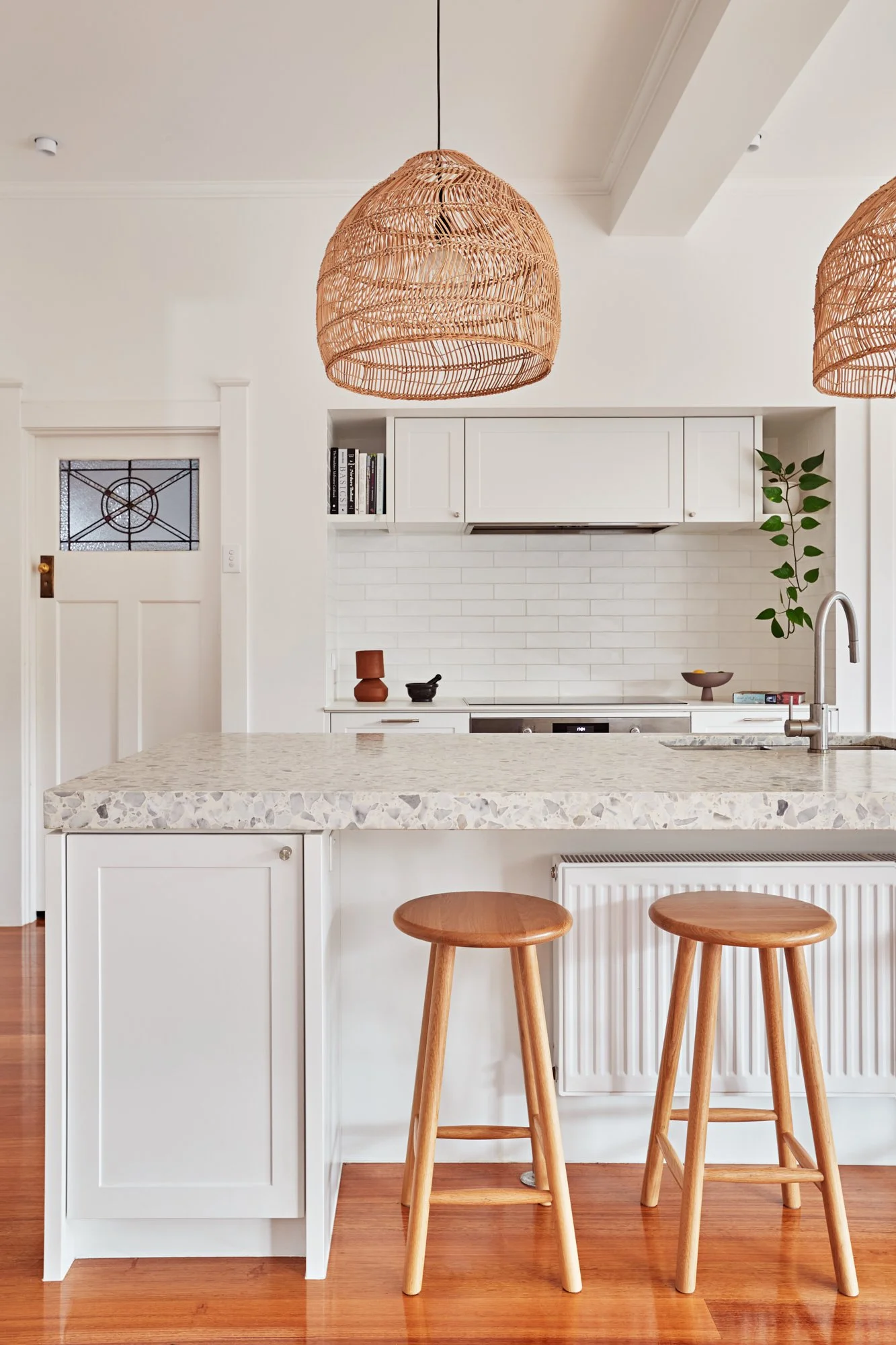 Kitchen island with terrazzo benchtop, timber stools and woven pendant lighting at Adella Court, Elwood.