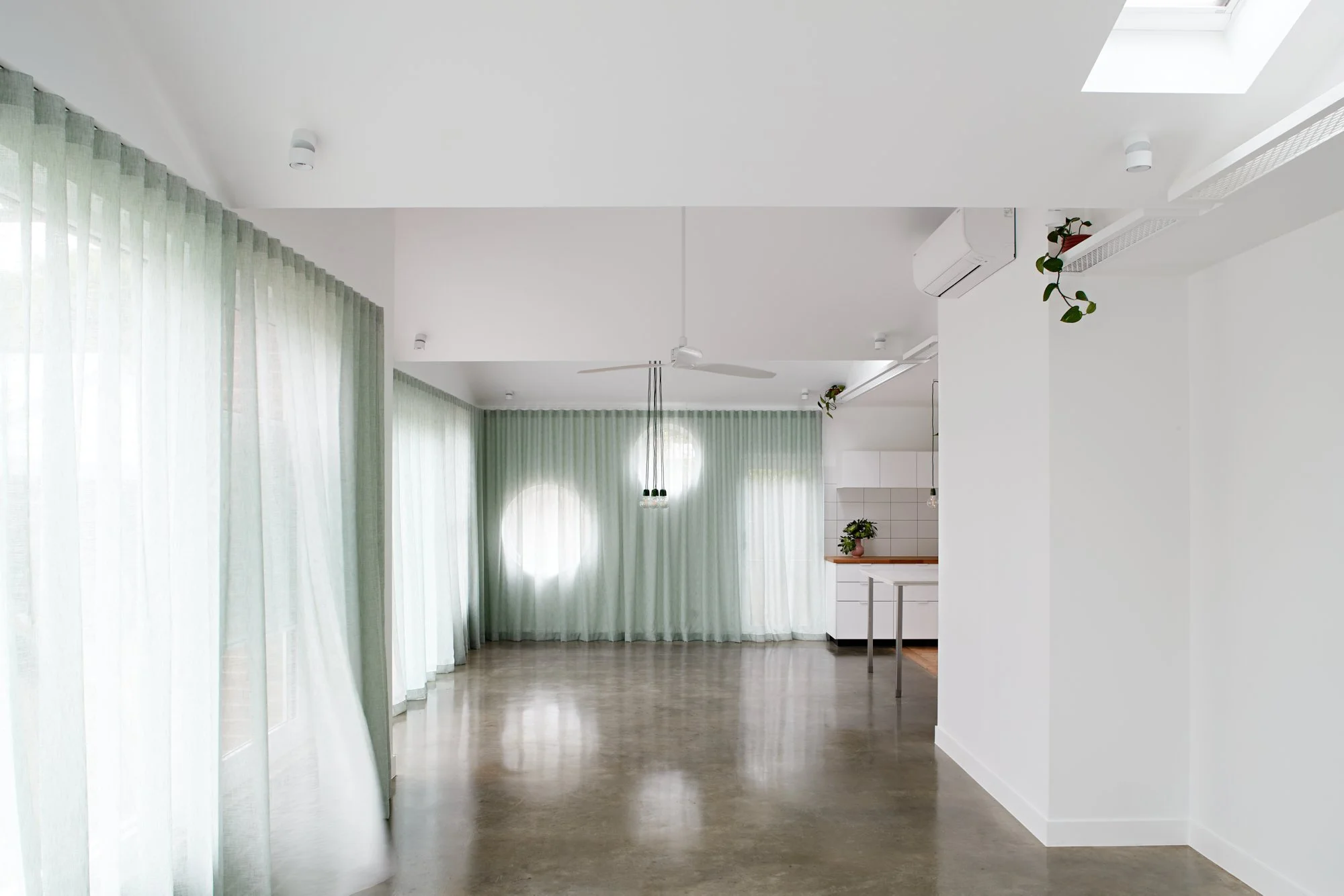 Light-filled open-plan interior of Northcote Green House with polished concrete floors and sheer green curtains.