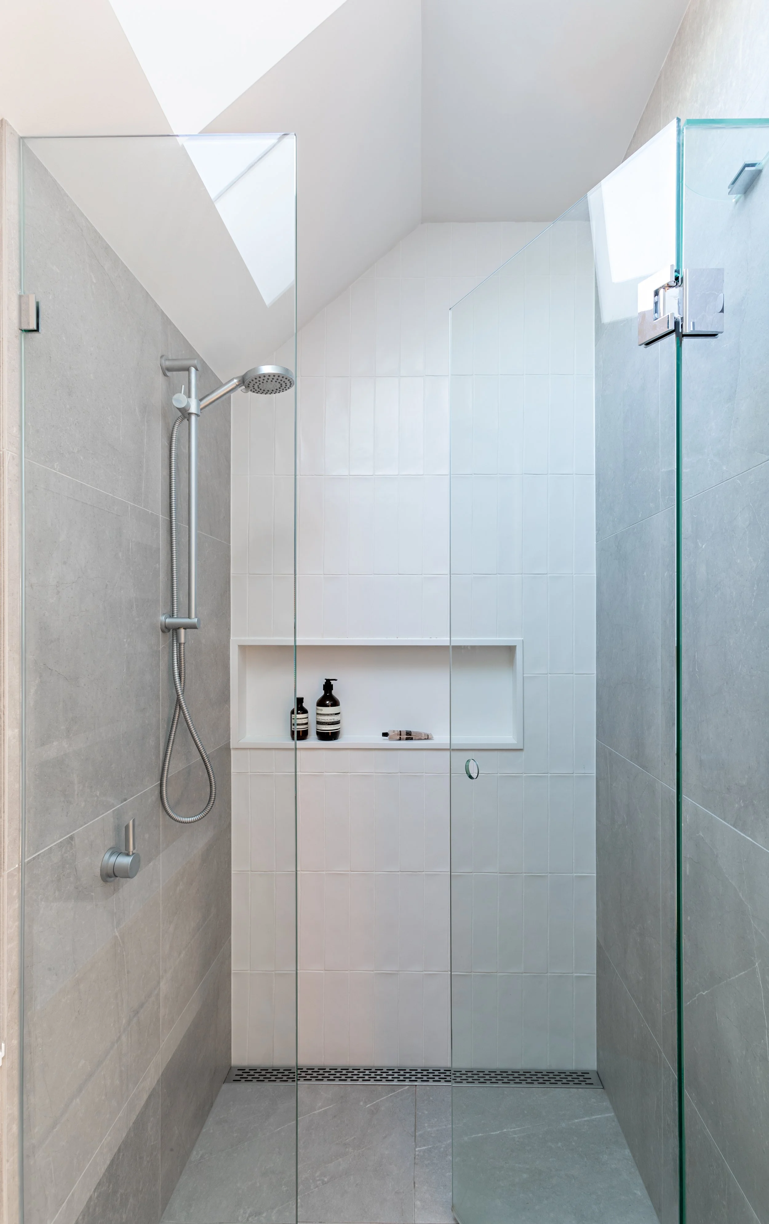 Walk-in shower with frameless glass screens, grey floor tiles and recessed storage niche at Brighton East House.