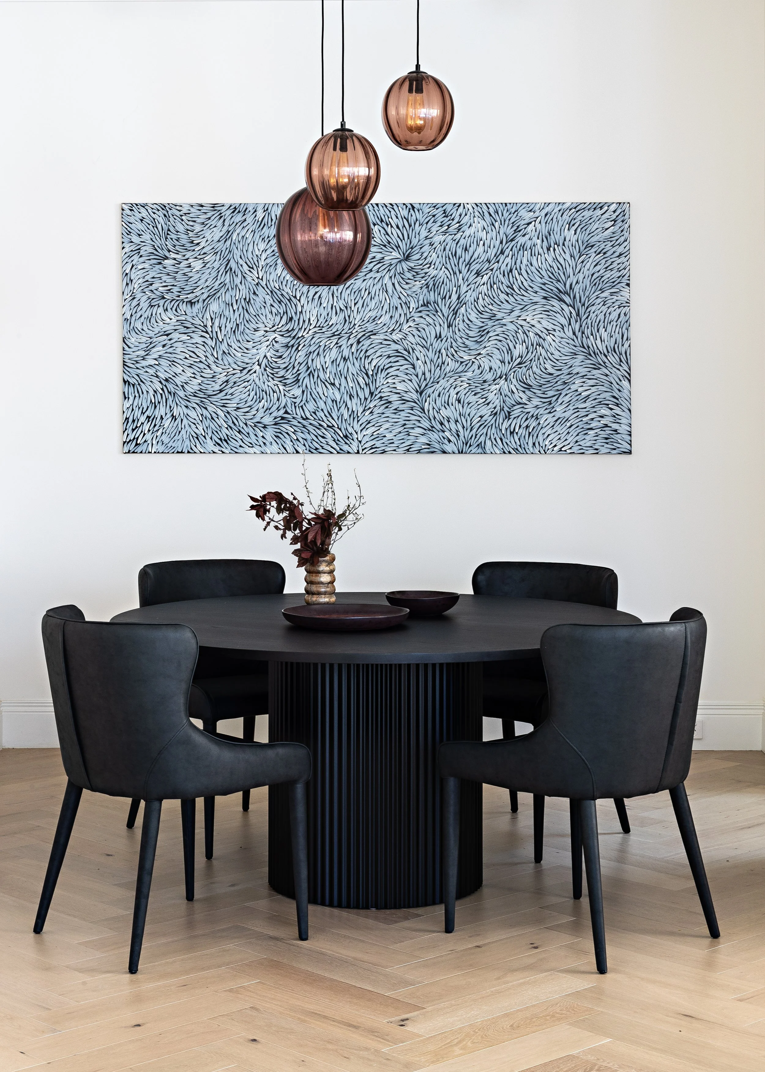 Brighton East House dining area with round black dining table, pendant lighting and contemporary artwork.