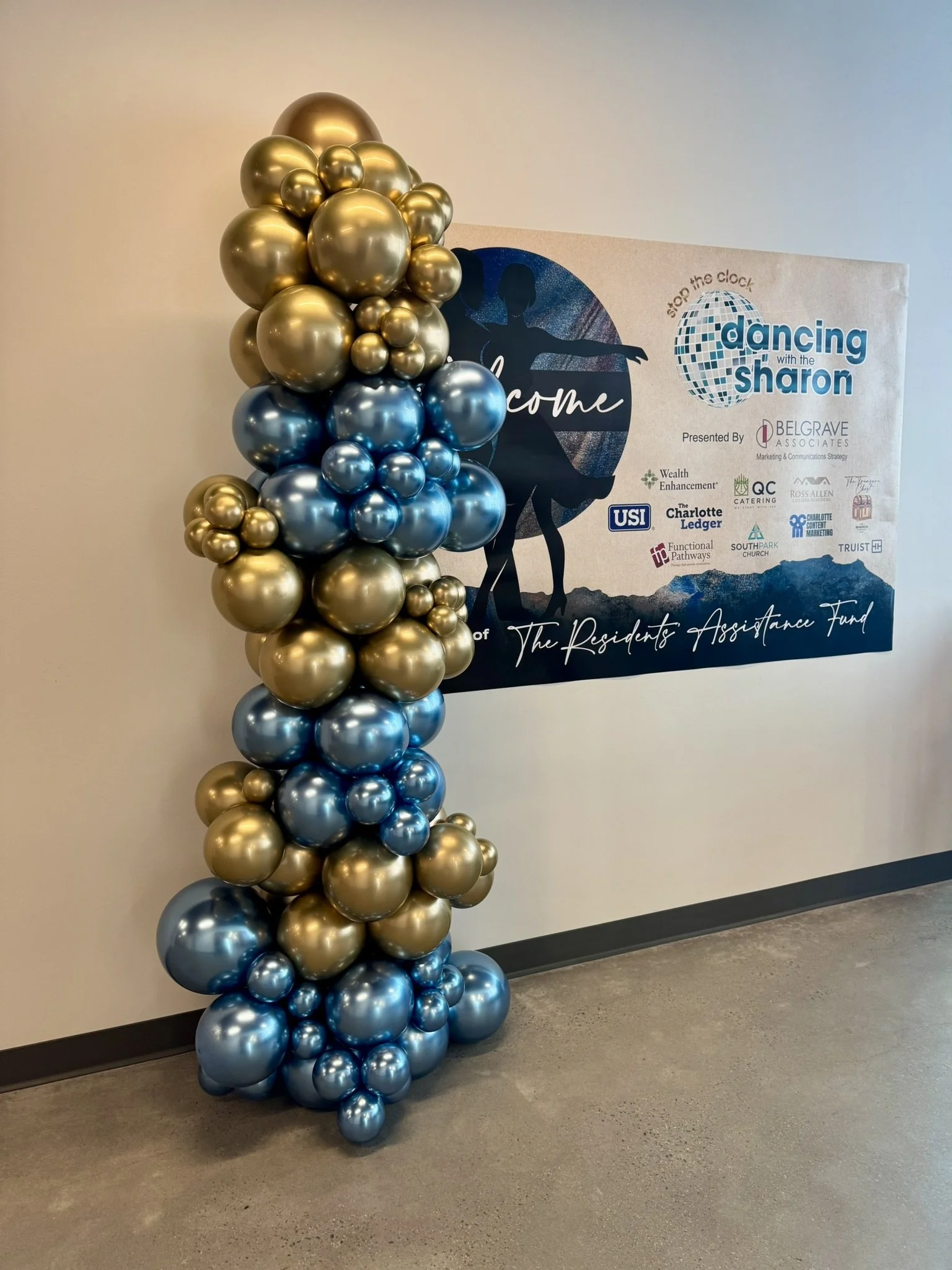 Decorative balloon column with gold and blue balloons standing next to a promotional backdrop for Dancing with the Sharon event.