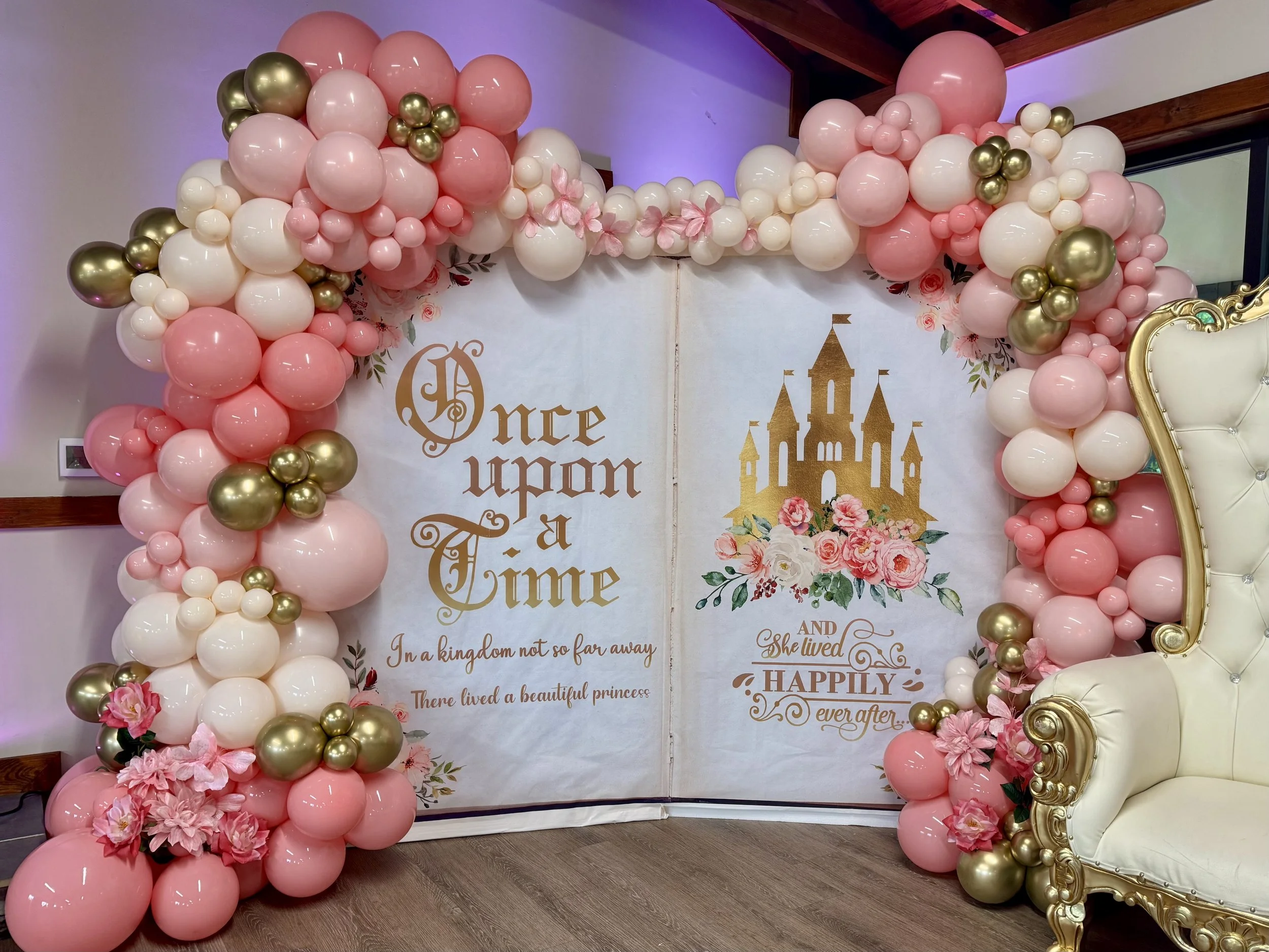 Whimsical fairytale balloon backdrop designed with blush pink, ivory, and metallic gold balloons accented by florals. Styled around a storybook backdrop that reads ‘Once Upon a Time’ and ‘Happily Ever After’, this balloon display is perfect for princ