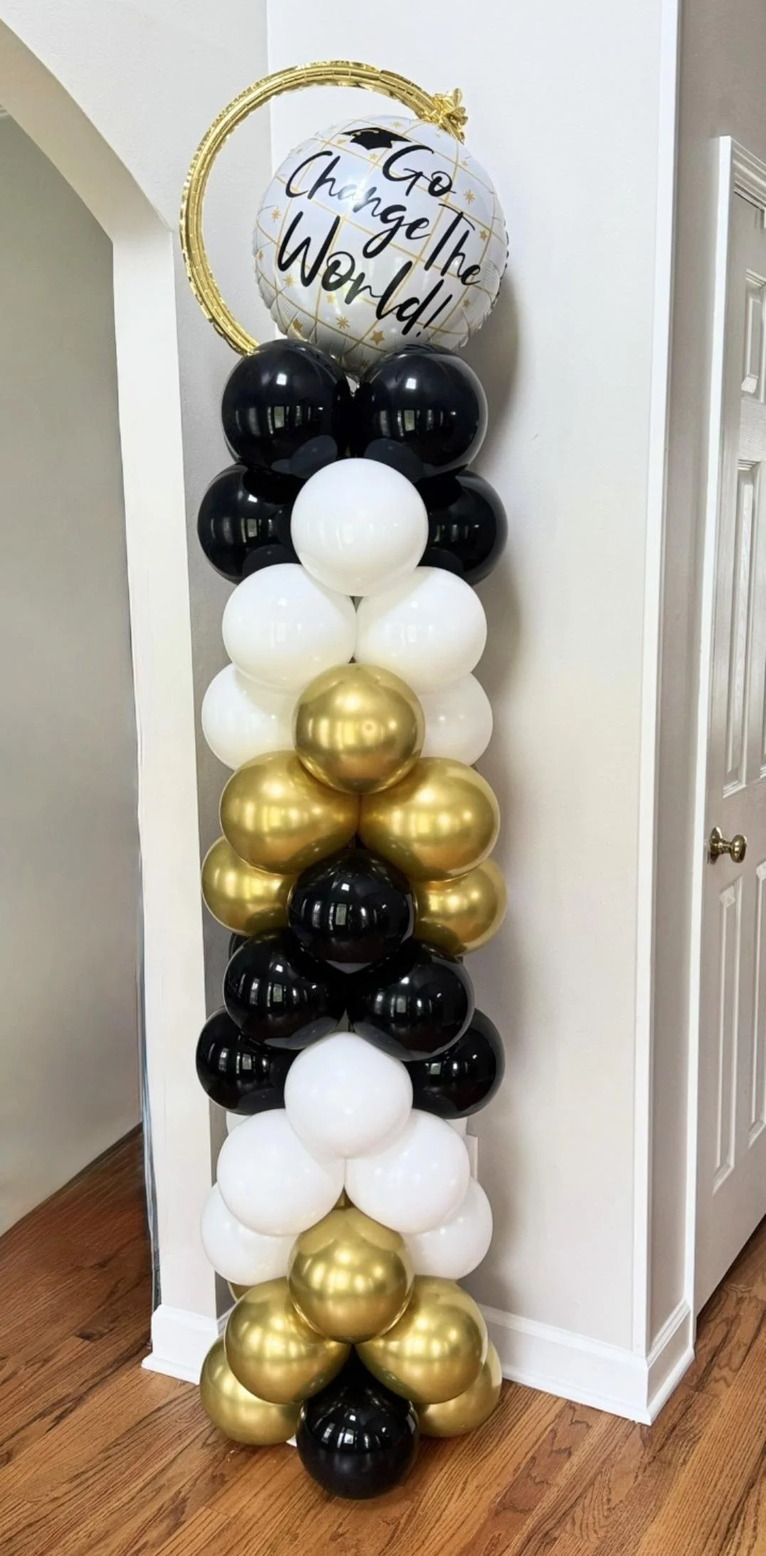 Graduation balloon column with black, white, and gold balloons topped by "Go Change The World" balloon.