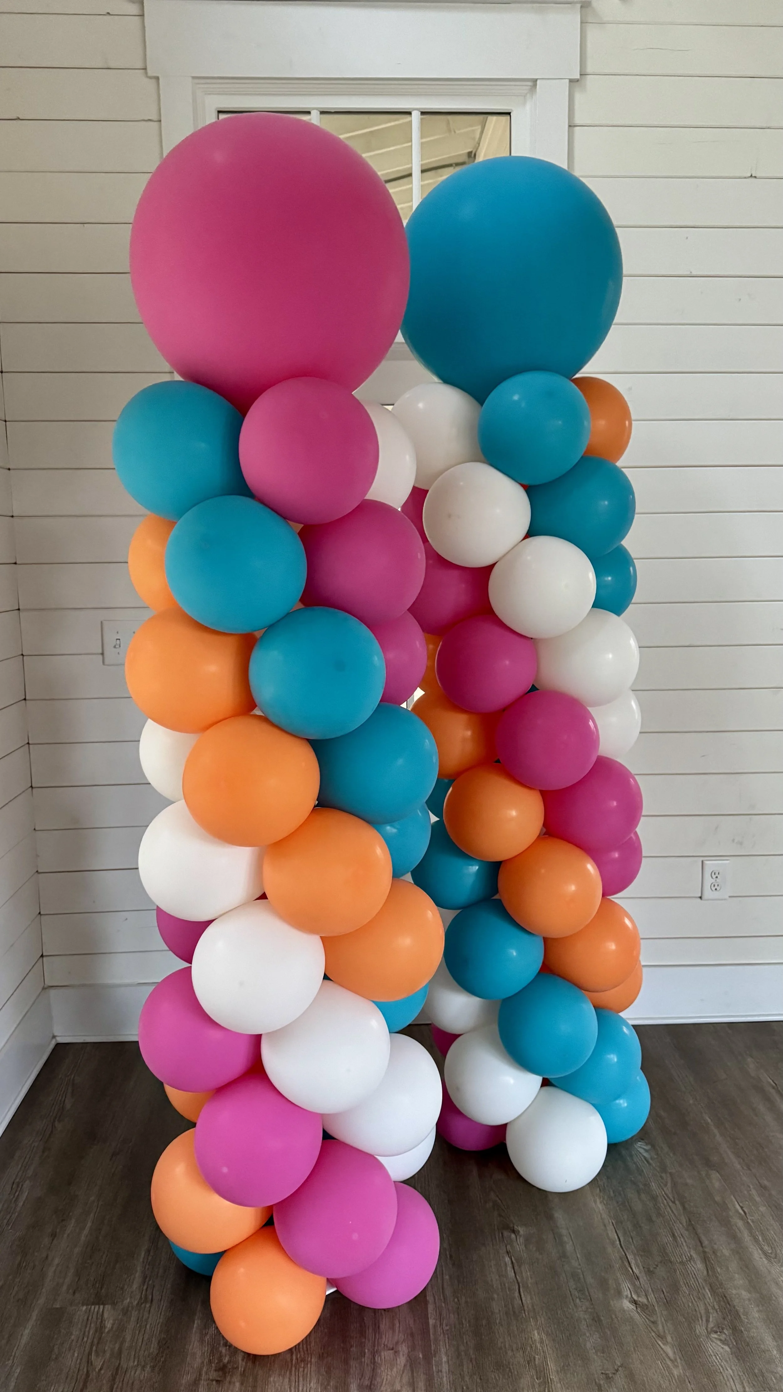 A balloon column including pink, blue, white, and orange for a luau theme.