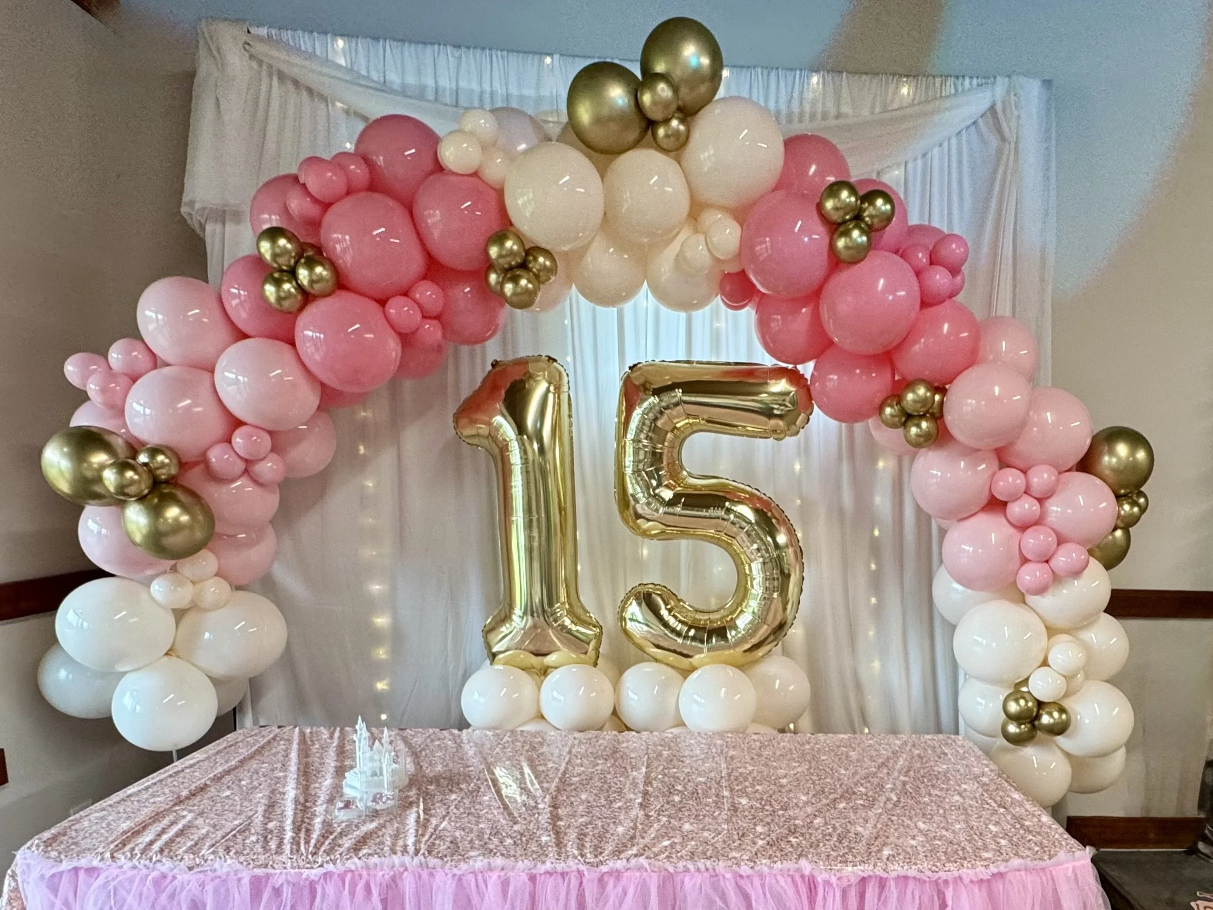 Stunning pink, white, and gold balloon arch with jumbo gold number balloons, perfect for a quinceañera, sweet 15, or milestone birthday celebration. Designed with a mix of balloon sizes for a full, luxurious look, this custom balloon display makes th