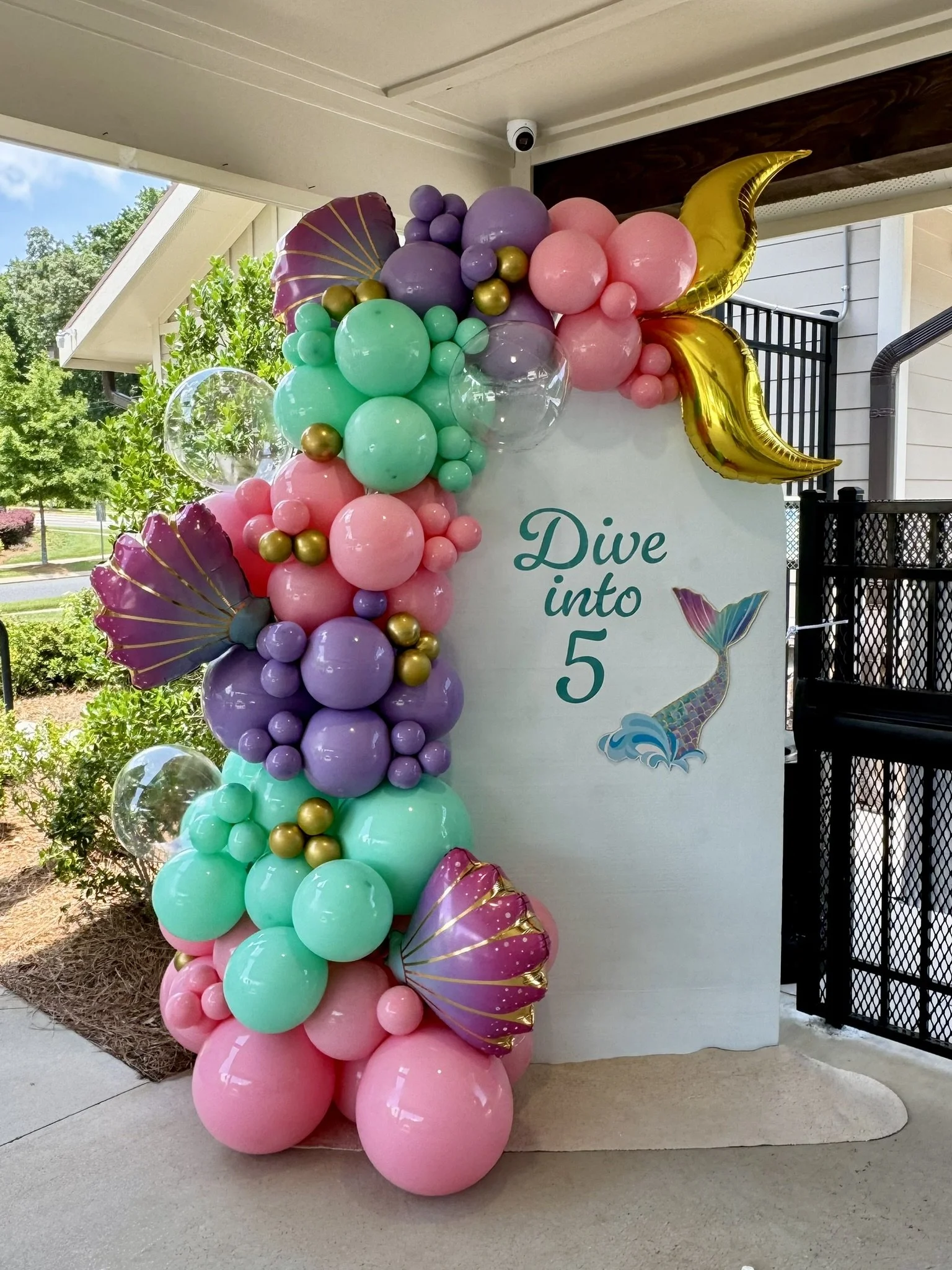Colorful balloon arch with purple, pink, mint green, and gold balloons, decorated with sea shell and mermaid theme, with the text "Dive into 5" and a mermaid illustration.