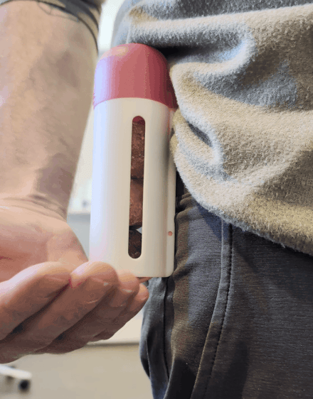 Person holding a pink and white device against their right side near the waist, with a clear vertical window showing the inside.