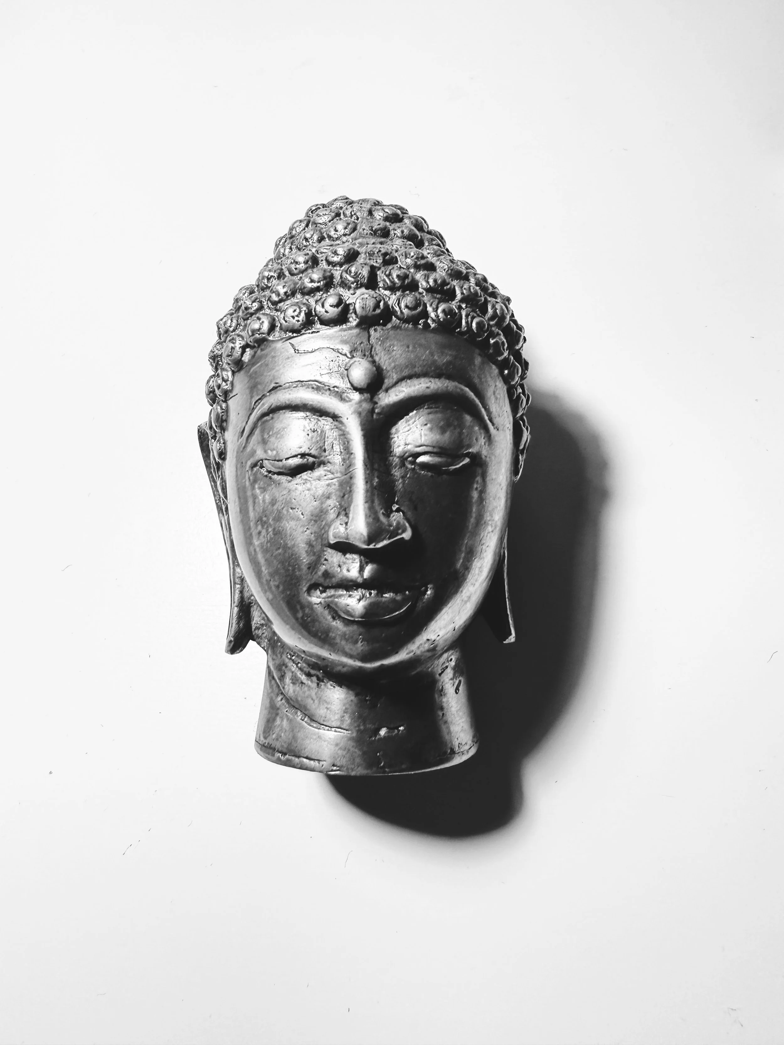 Black and white image of a Buddha head sculpture on a light background.