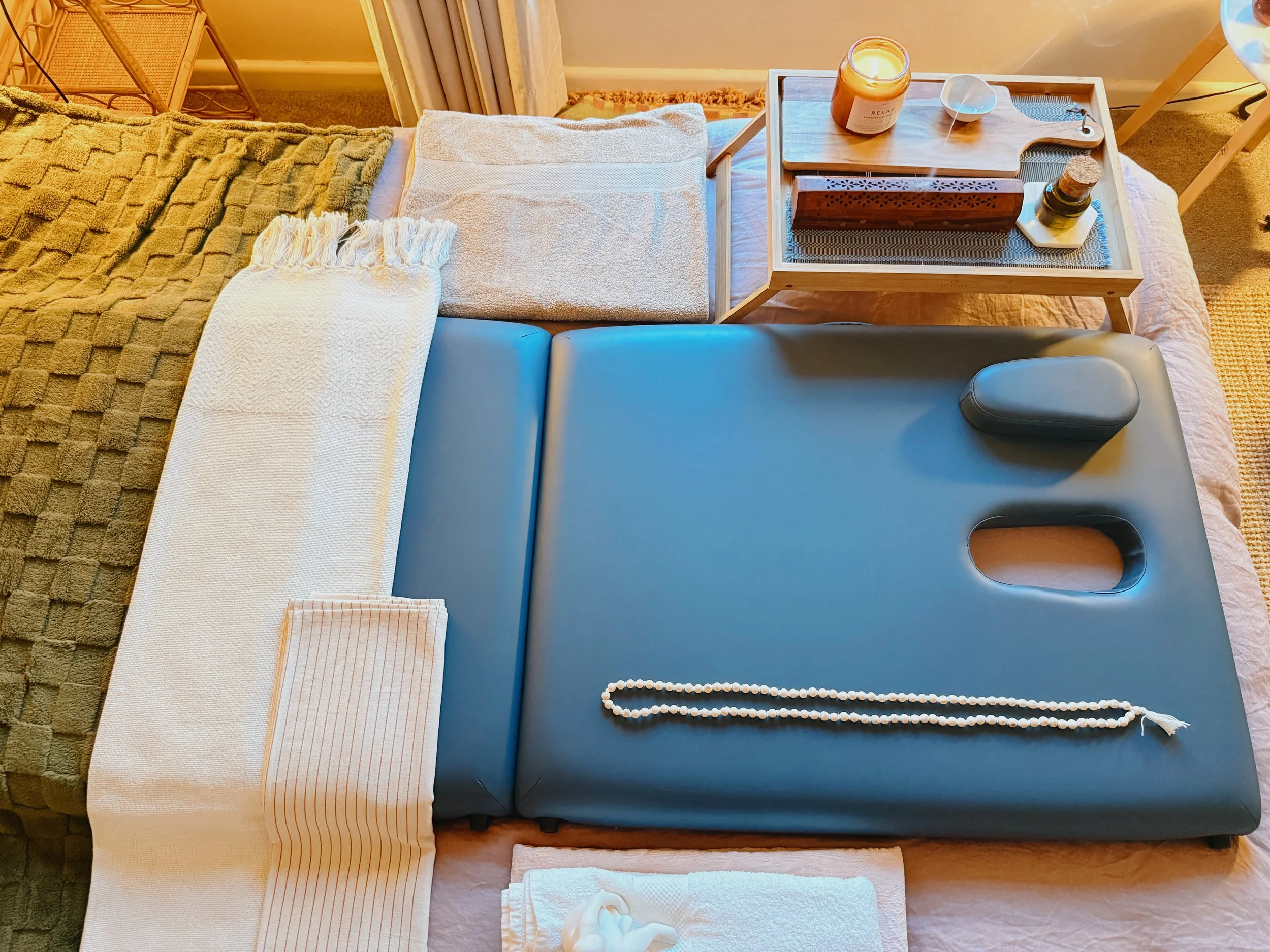 Massage therapy setup with a massage table, cozy blankets, pillows, candles, and relaxing decor on a tray.