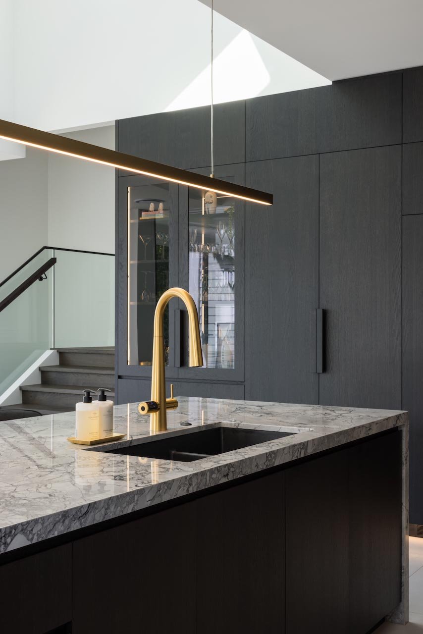 Kitchen island bench in grey marble with gold tap and blade light above.