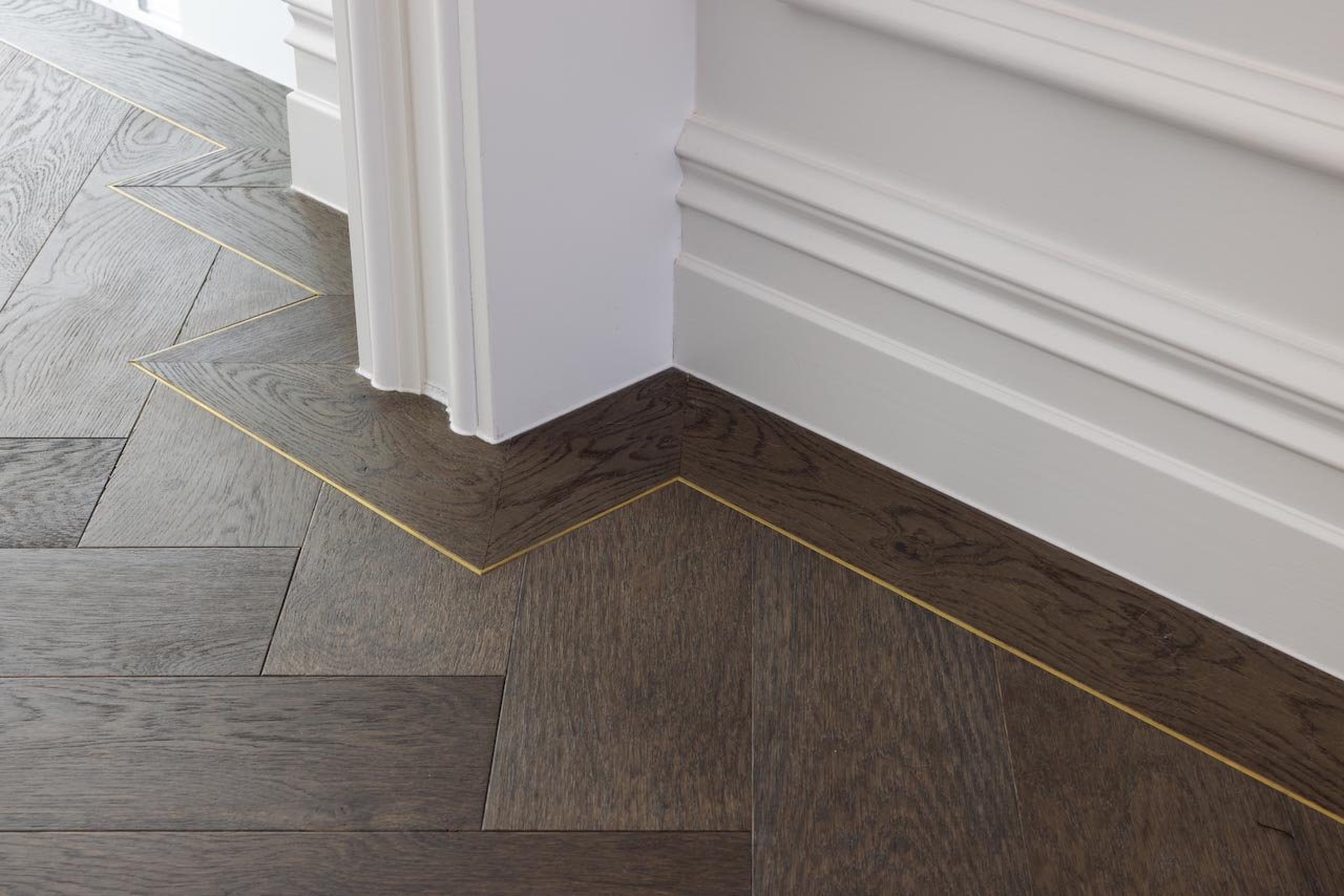 Detail showing the oak herringbone floor with brass trim and a colonial moulding painted white.