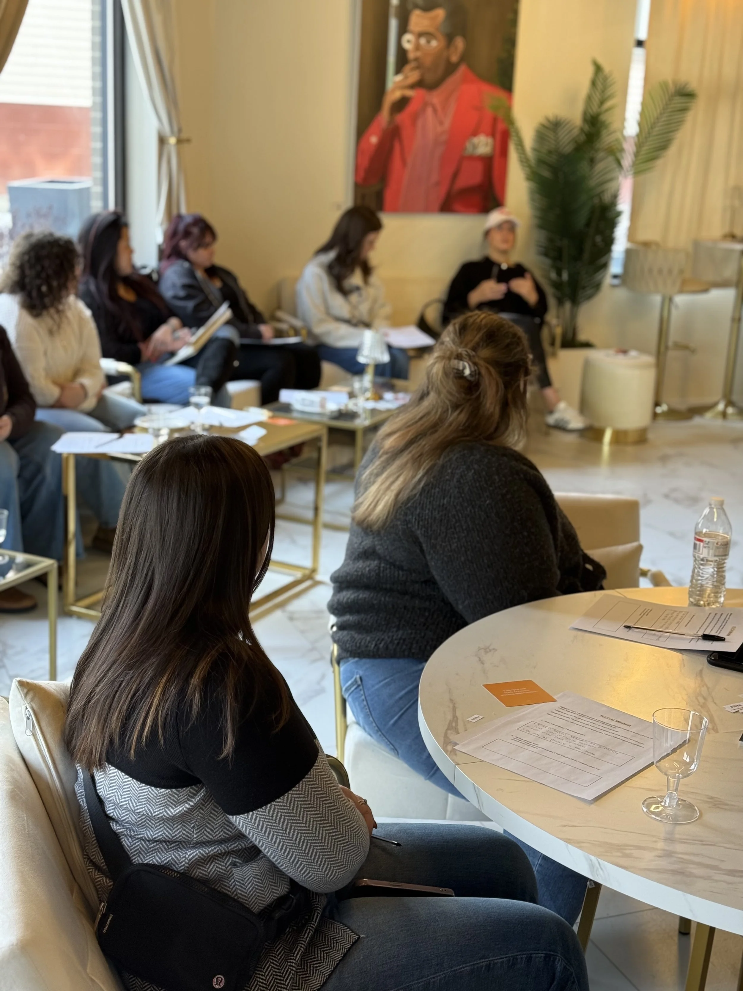 Group of women attending Jentle Land Mark's Invest in You event in a well-lit room with a large colorful portrait on the wall, a tall plant, and modern furniture at the Jones Collective in Allentown, PA.