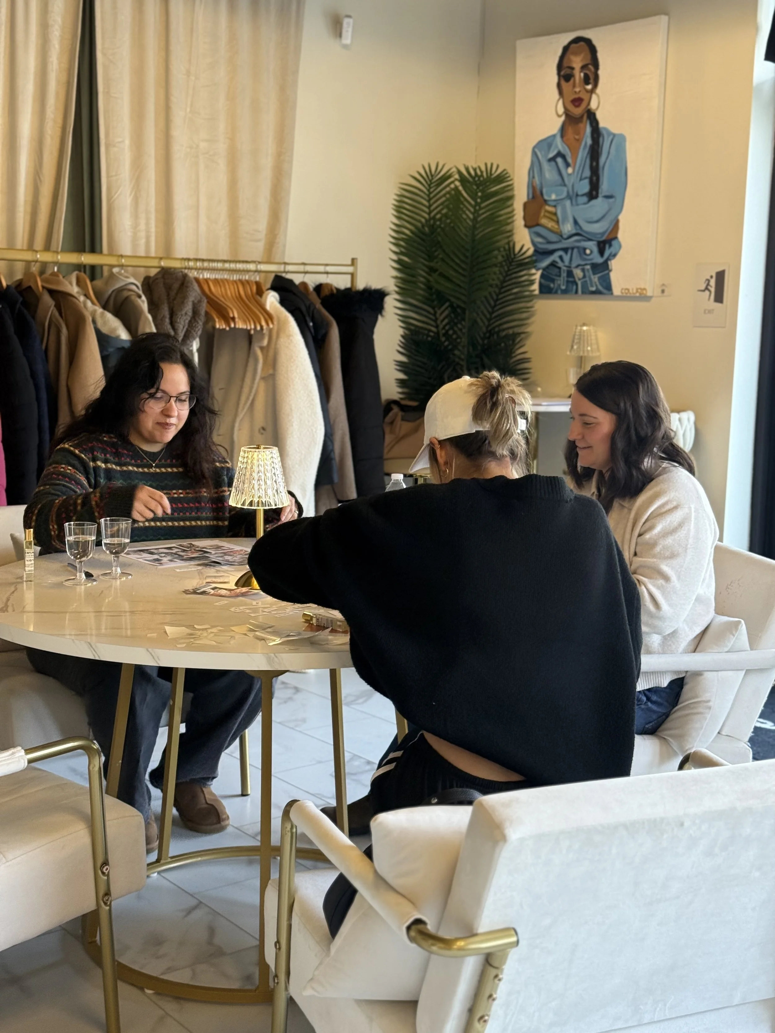 Four diverse women sitting around a table creating 2026 personal vision boards in a cozy, well-lit room with clothing racks and a colorful portrait on the wall at the Jones Collective in Allentown, PA for Jentle Land Mark event.