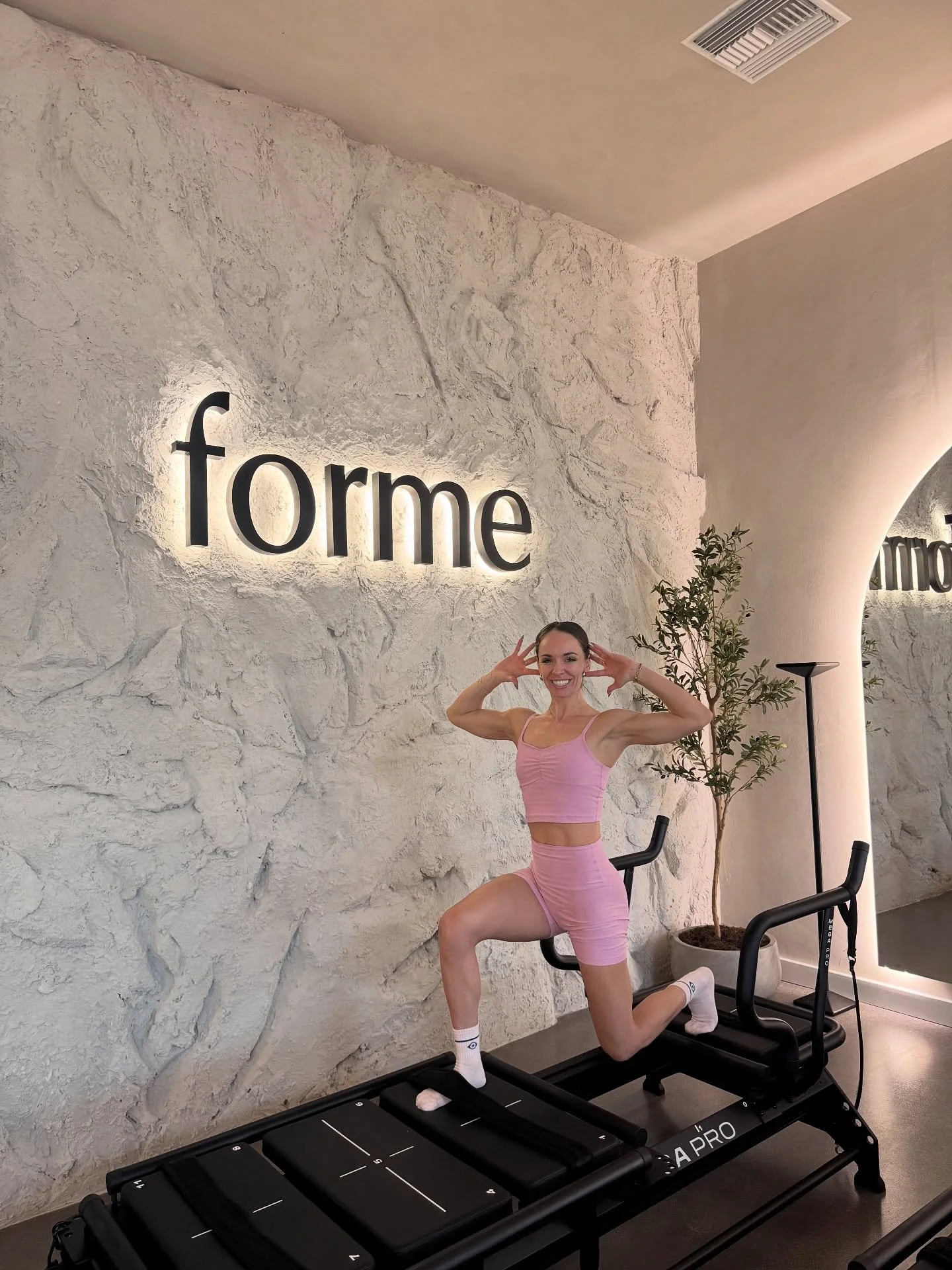 A member in a lunge on a Lagree machine in front of the lit forme wall at Forme Burbank